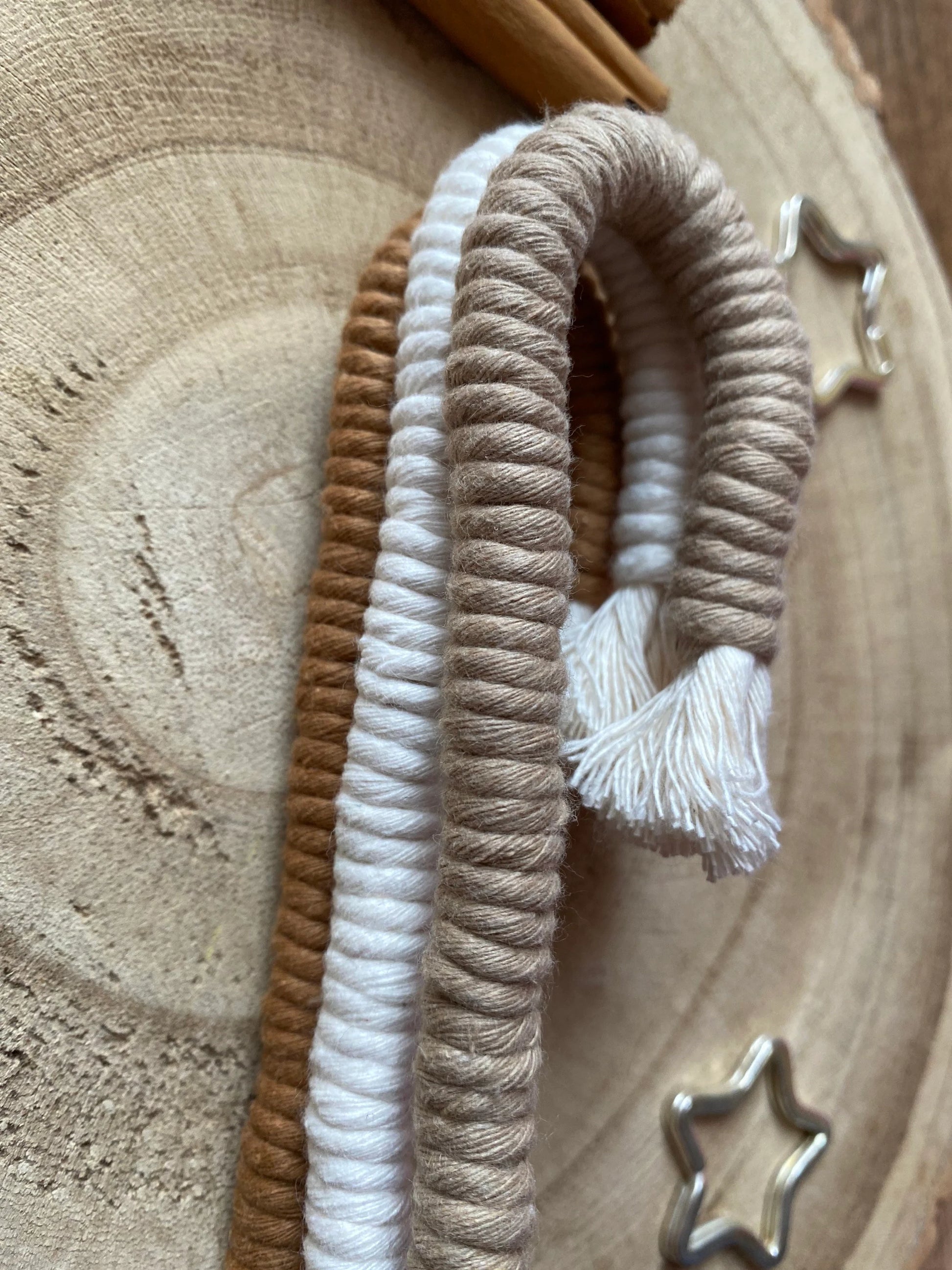 A close up of a set of three Christmas candy cane shaped macrame ornaments in beige, white, and brown colours with tassels, stacked on top of each other.