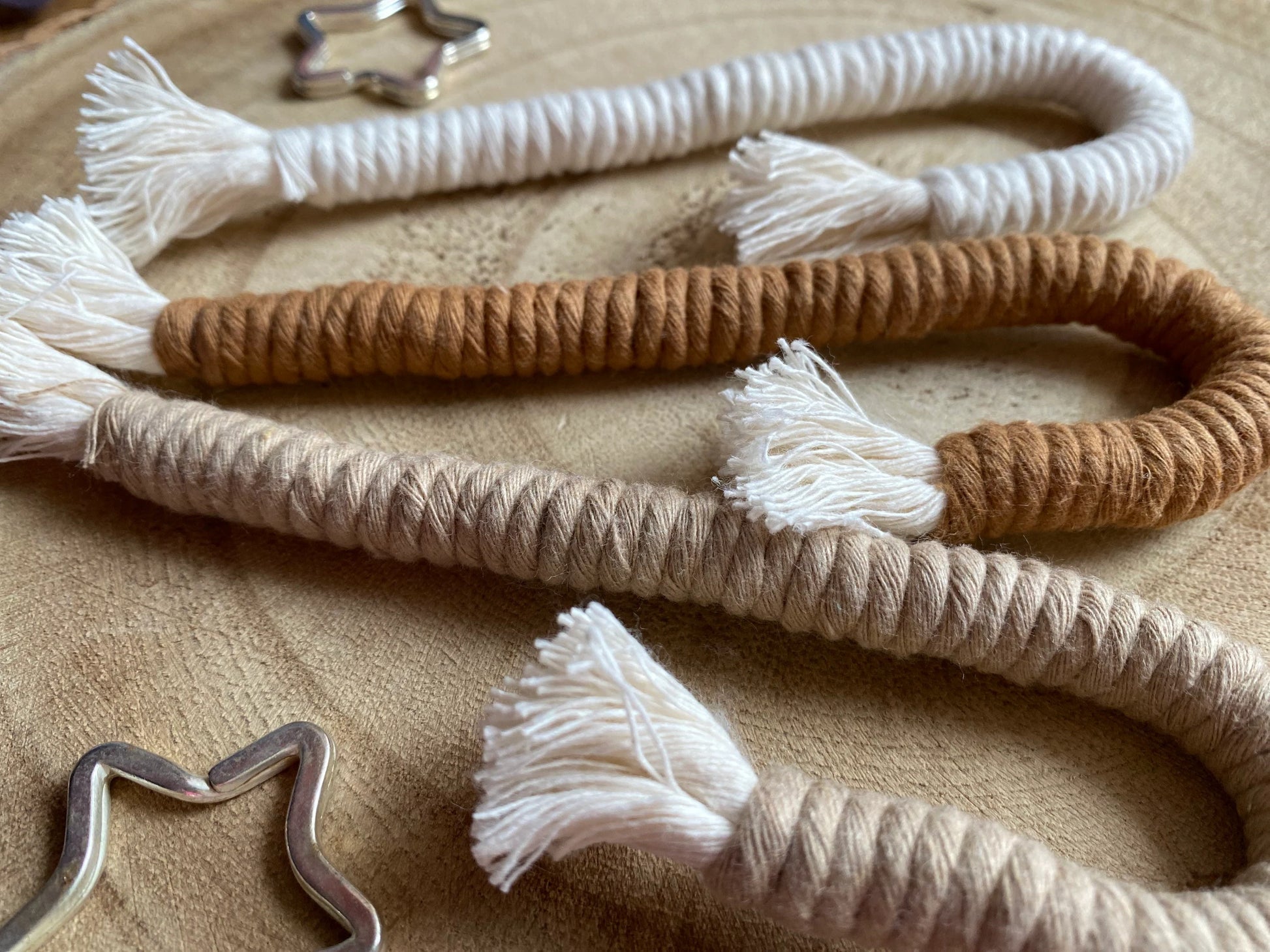 A close up angled image of a set of three Christmas candy cane shaped macrame ornaments in beige, white, and brown colours with tassels, displayed on a wooden surface.