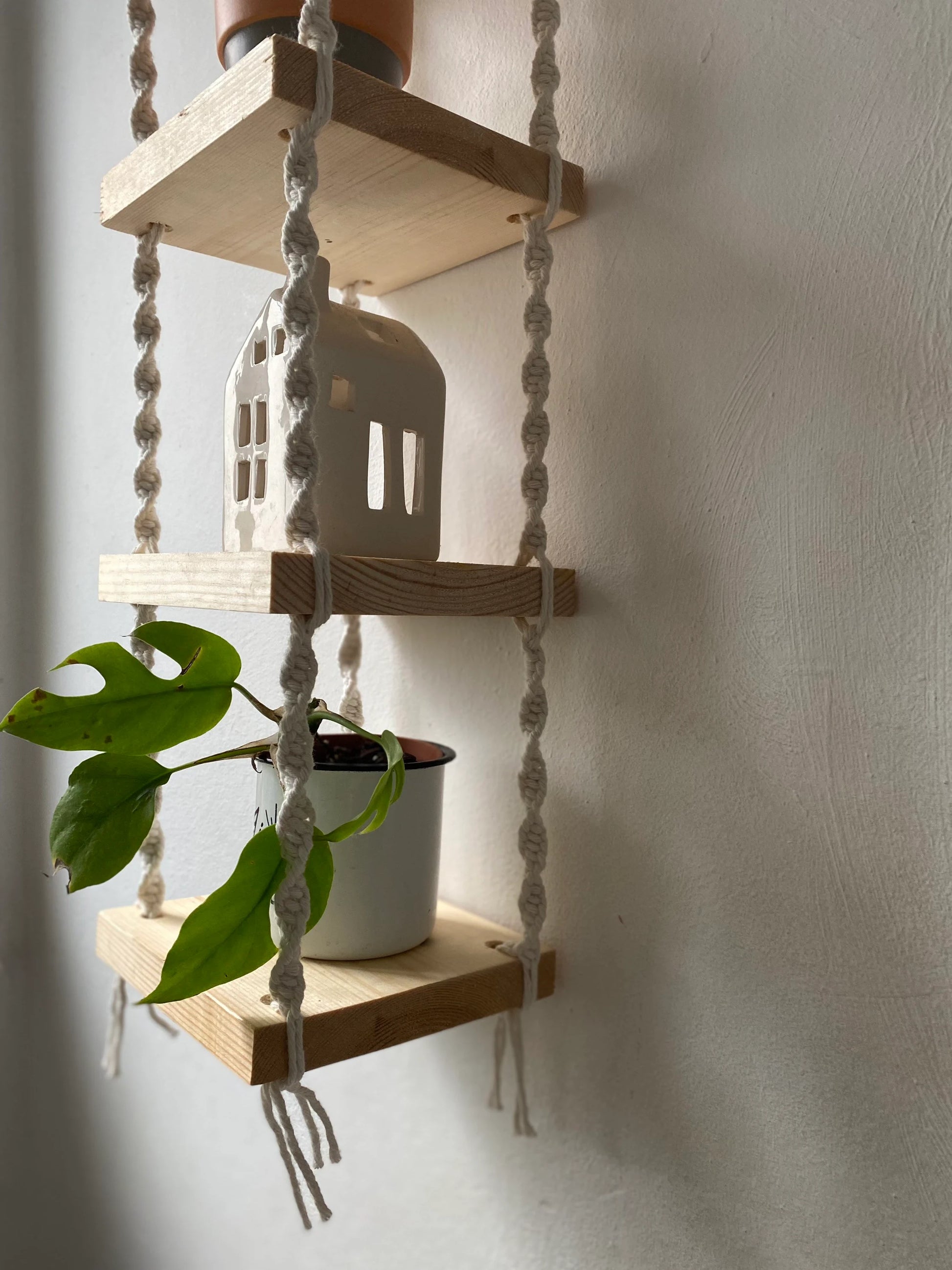 Handmade macrame rope shelves, made with small square wooden shelves, held together with natural knotted rope. Displayed hanging on a white wall.