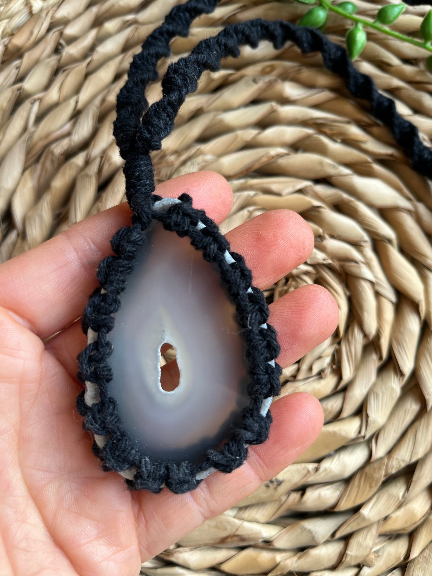 Hand holding natural agate slice in black macrame necklace