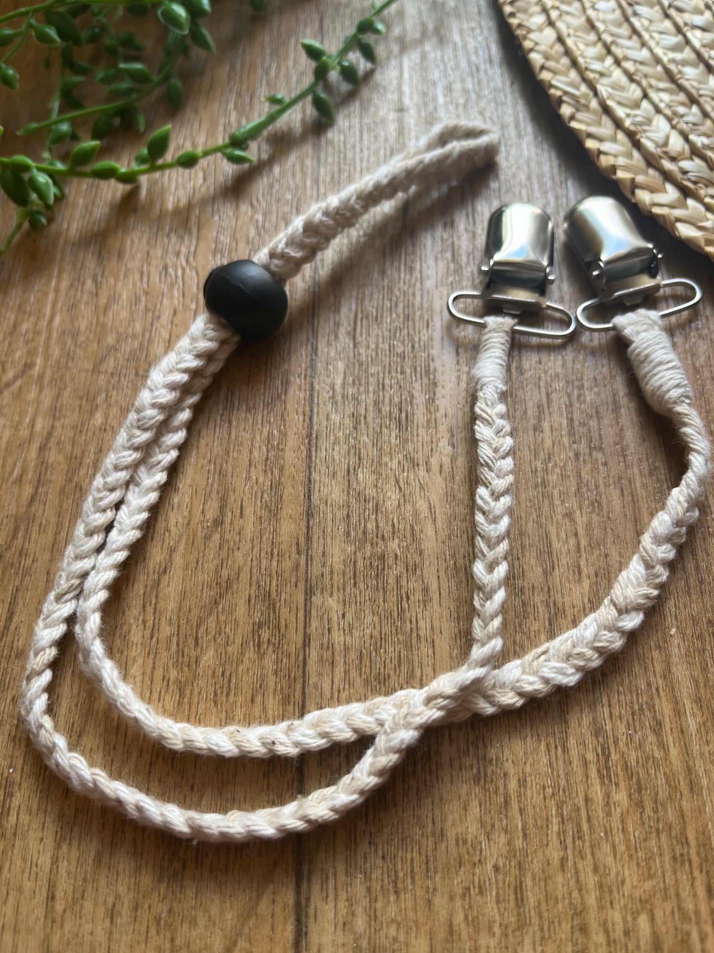 Braided macrame chin strap lanyard with metal clips and black toggle on a wooden surface
