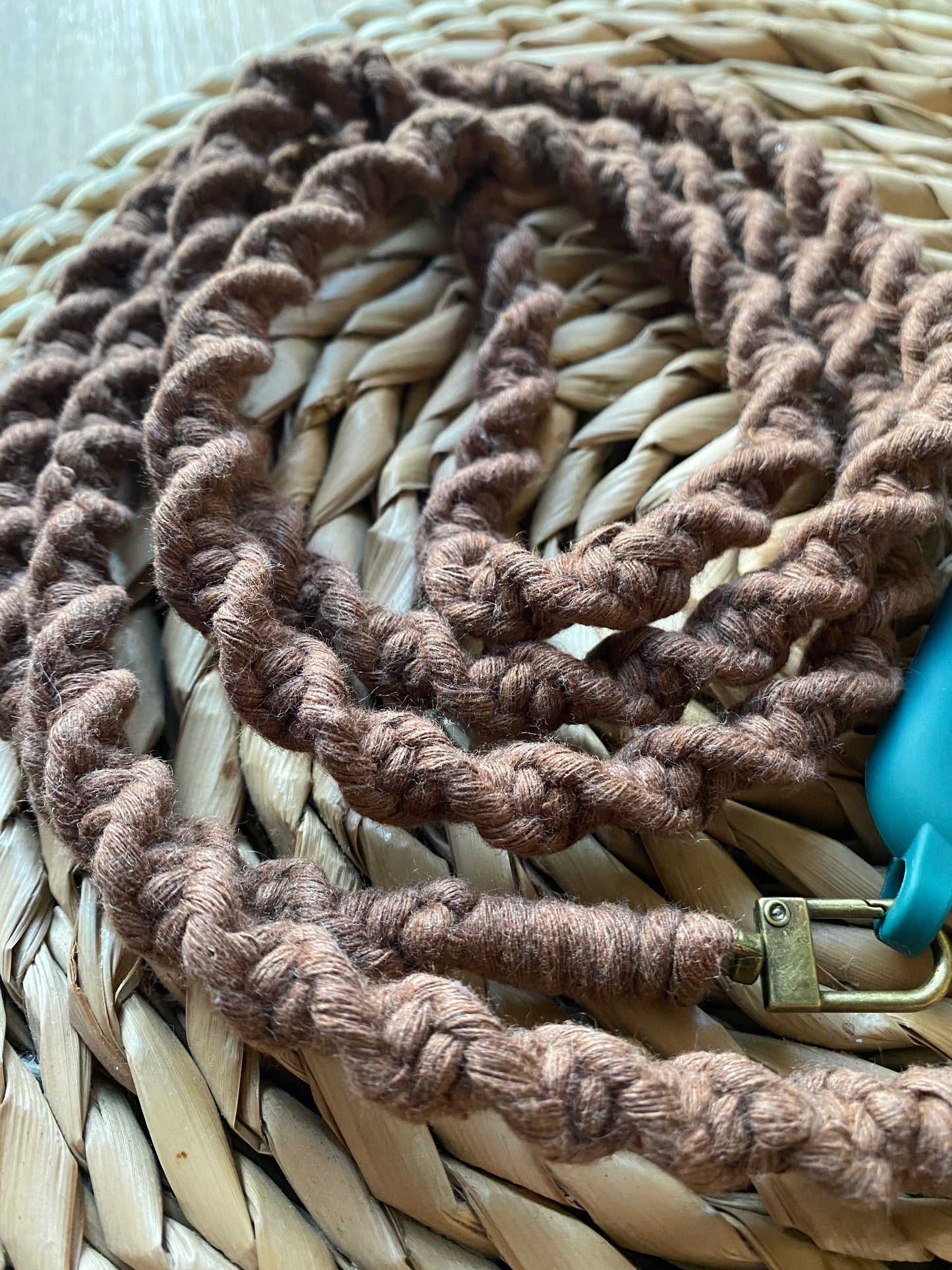 Close up of the twisted knot pattern on a macrame crossbody phone strap, made with mocha brown recycled cotton yarn, on a woven mat.