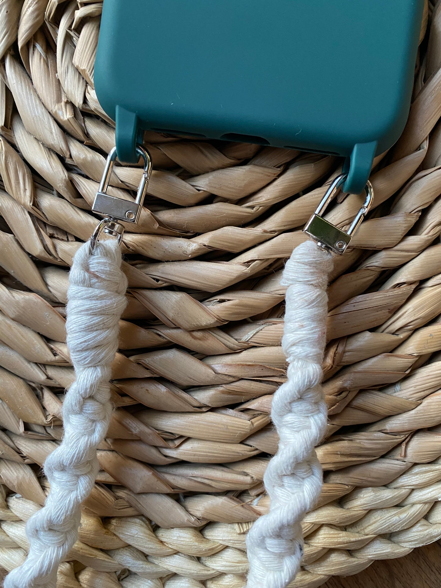 Close up of a macrame phone strap attached to the bottom of a green phone case with two silver clips on either side.
