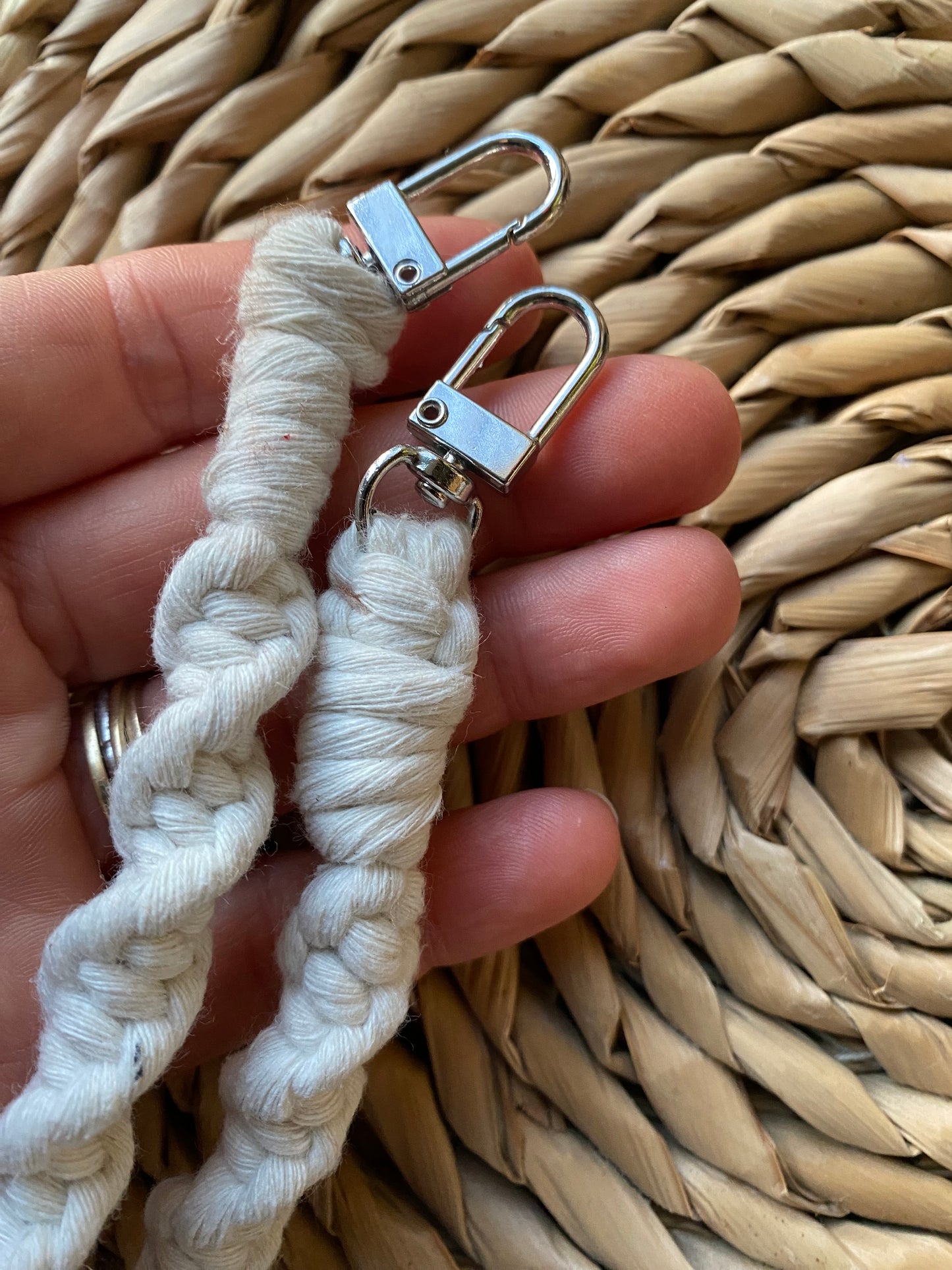 a hand holding the silver clips on the ends of a macrame knotted crossbody phone strap made with natural cotton.