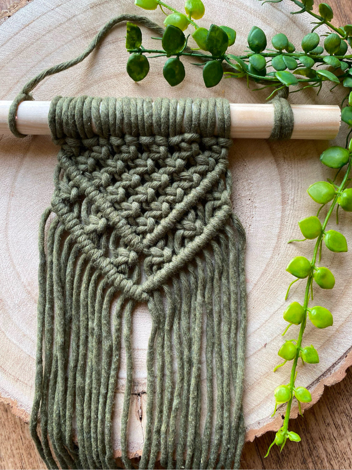 A small boho style macrame wall hanging, made with recycled cotton yarn on a wooden dowel.