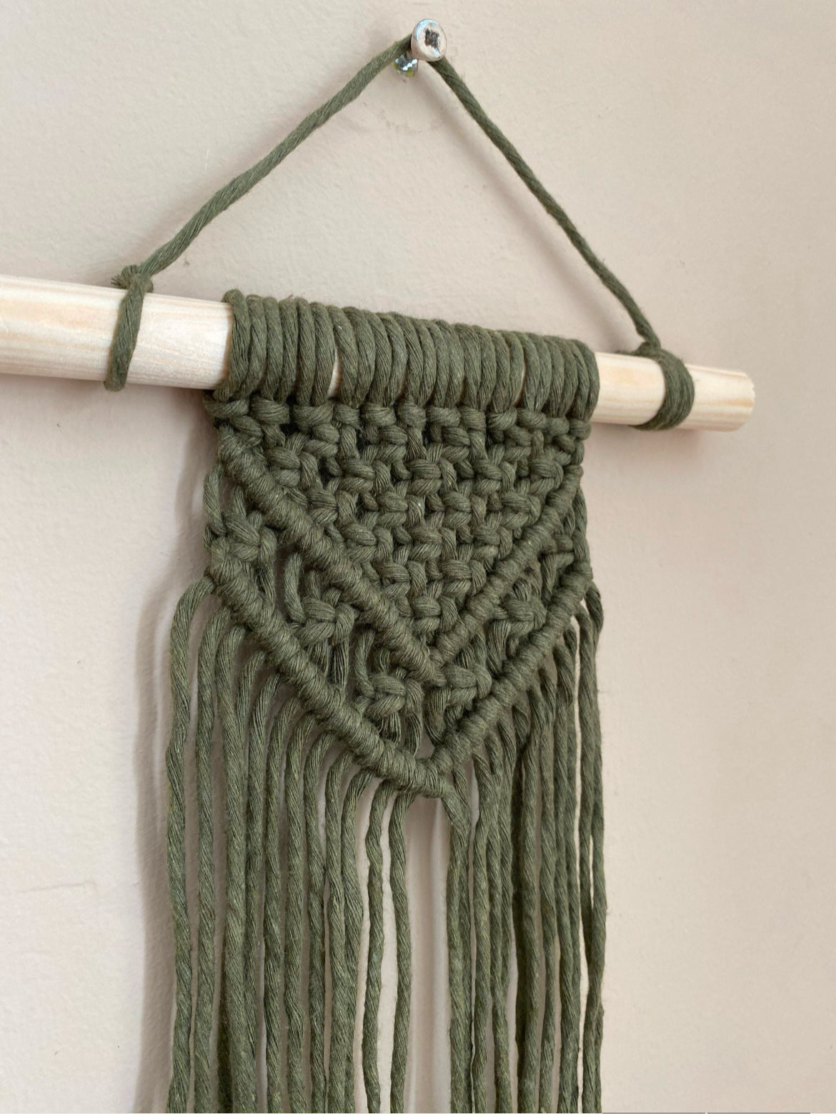 Handmade macrame wall hanging made with avocado green recycled cotton cord on a solid wooden dowel.