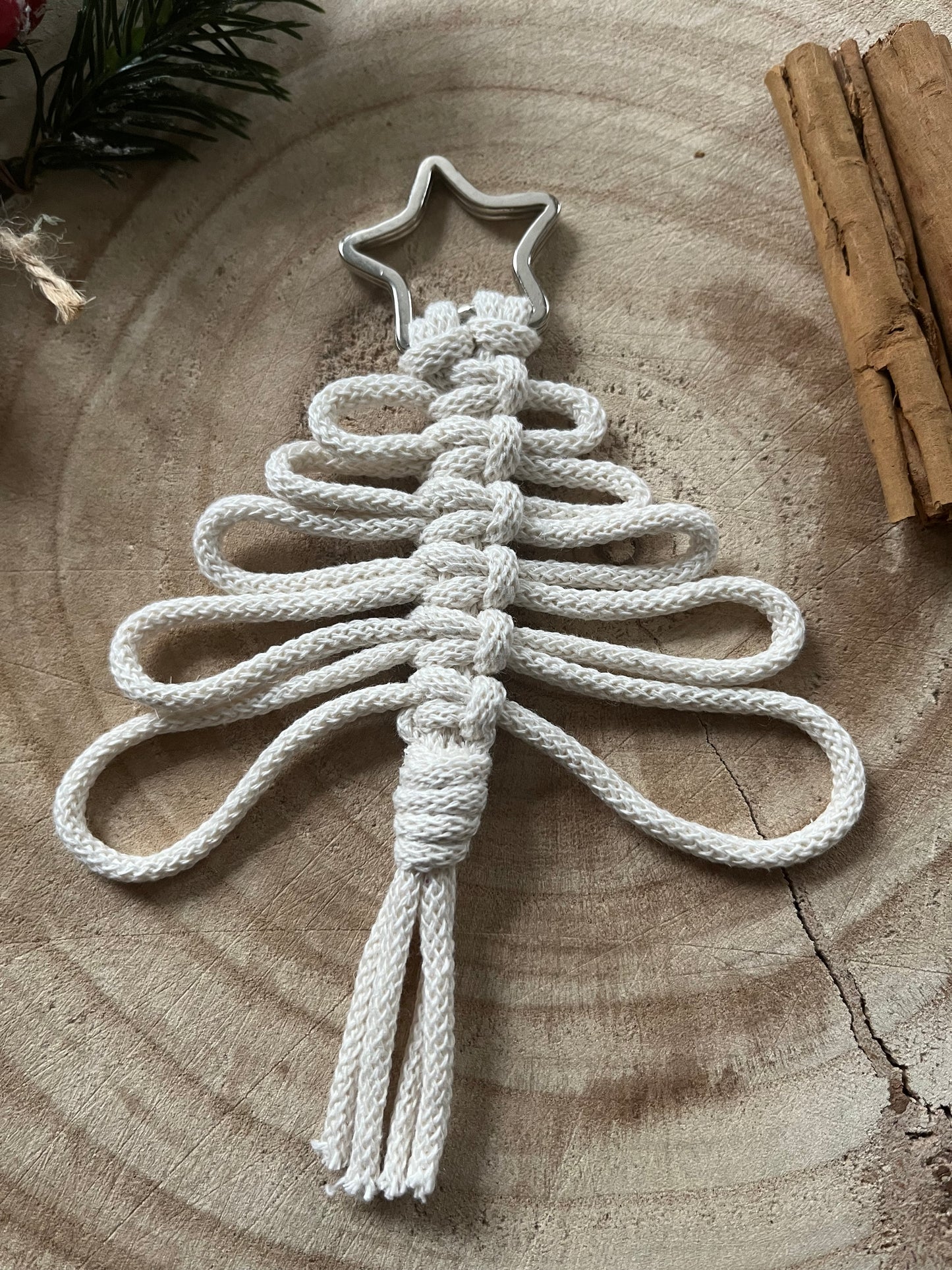 Handmade macrame Christmas tree decoration made with recycled cotton yarn on a metal split ring, on a wooden surface.