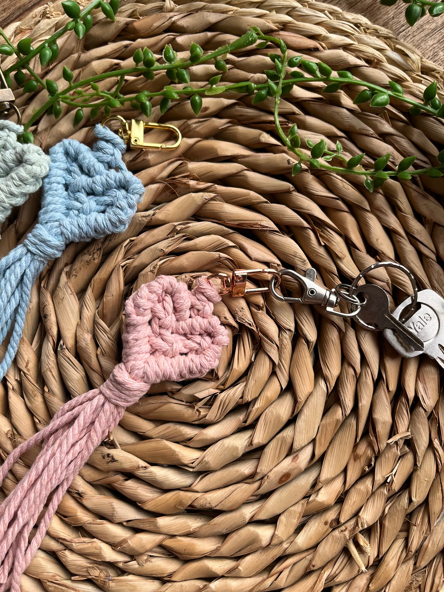 Handmade macrame heart shaped keychains, image focuses on a pink keychain attached to a small set of keys. Just seen on the left hand side are blue and green keychains too.