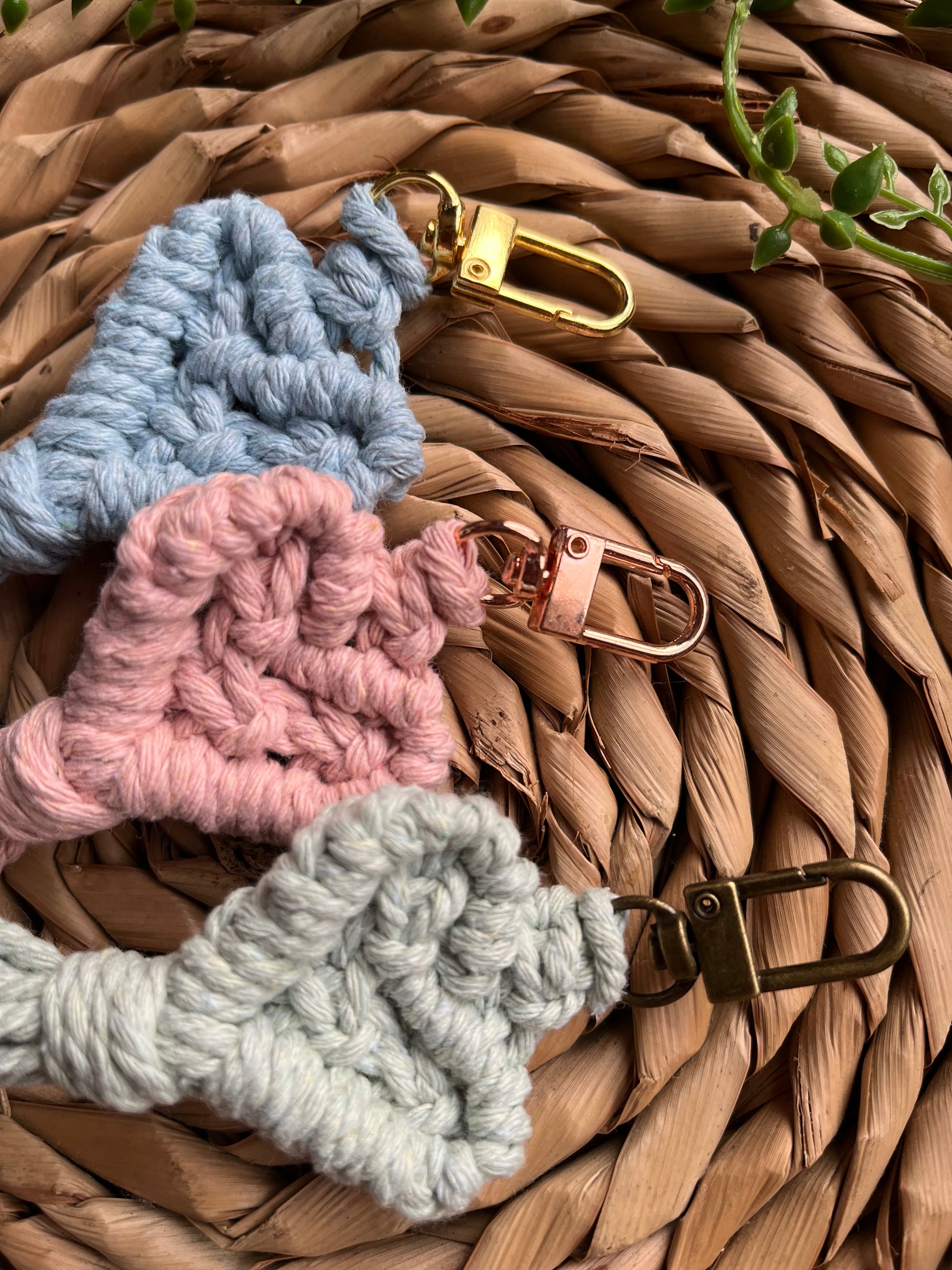 Three handmade macrame heart shaped keychains in pastel colours made with recycled cotton and metal clasps in different colours.