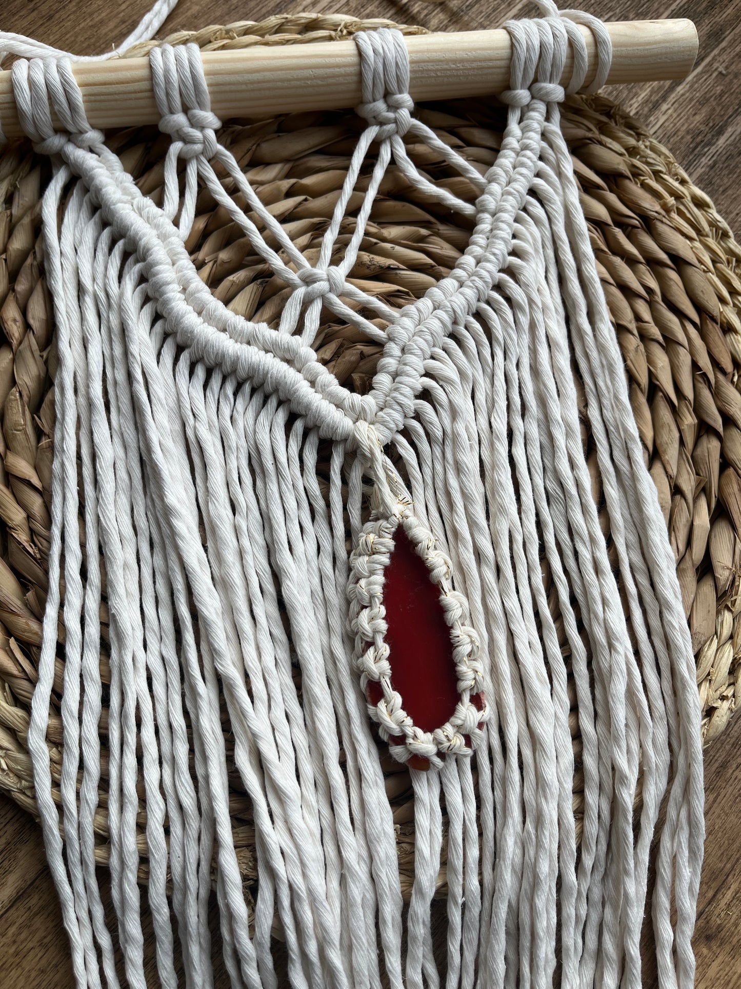 Macrame Wall Hanging, made with natural recycled cotton yarn on a wooden dowel, featuring a red agate slice. Displayed laid flat on a wicker mat.