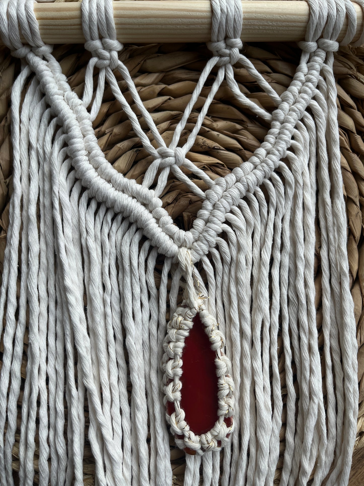 Macrame Wall Hanging, made with natural recycled cotton yarn on a wooden dowel, featuring a red agate slice. Displayed laid flat on a wicker mat.