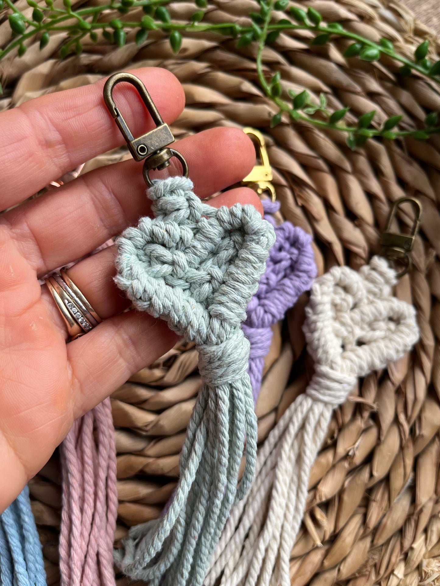 A hand holding a green heart shaped macrame keychain made with recycled cotton and an antique metal coloured clasp.