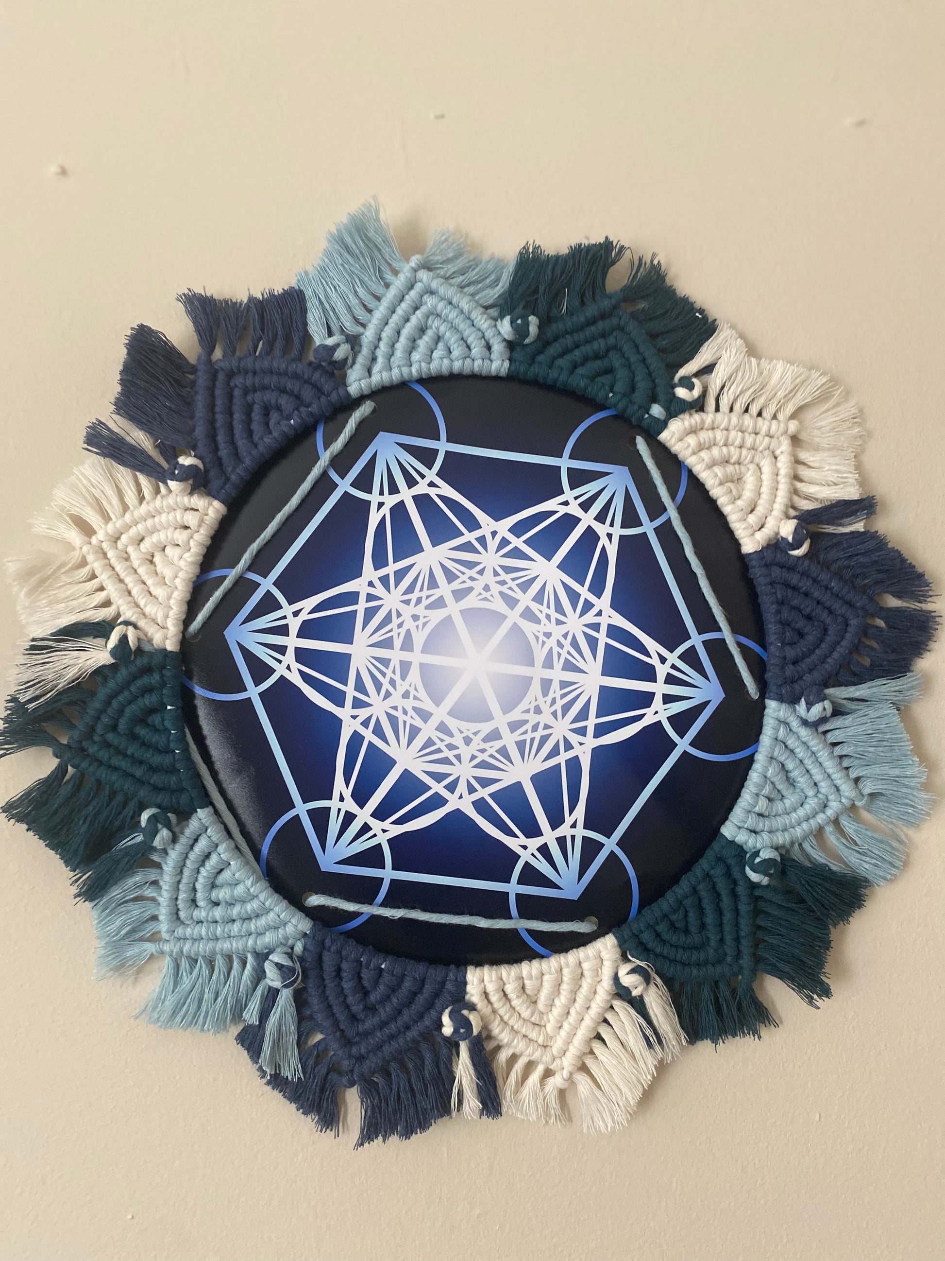 A macrame mandala frame knotted with blue and white yarn, surrounds a Metatron’s Cube geometric print.