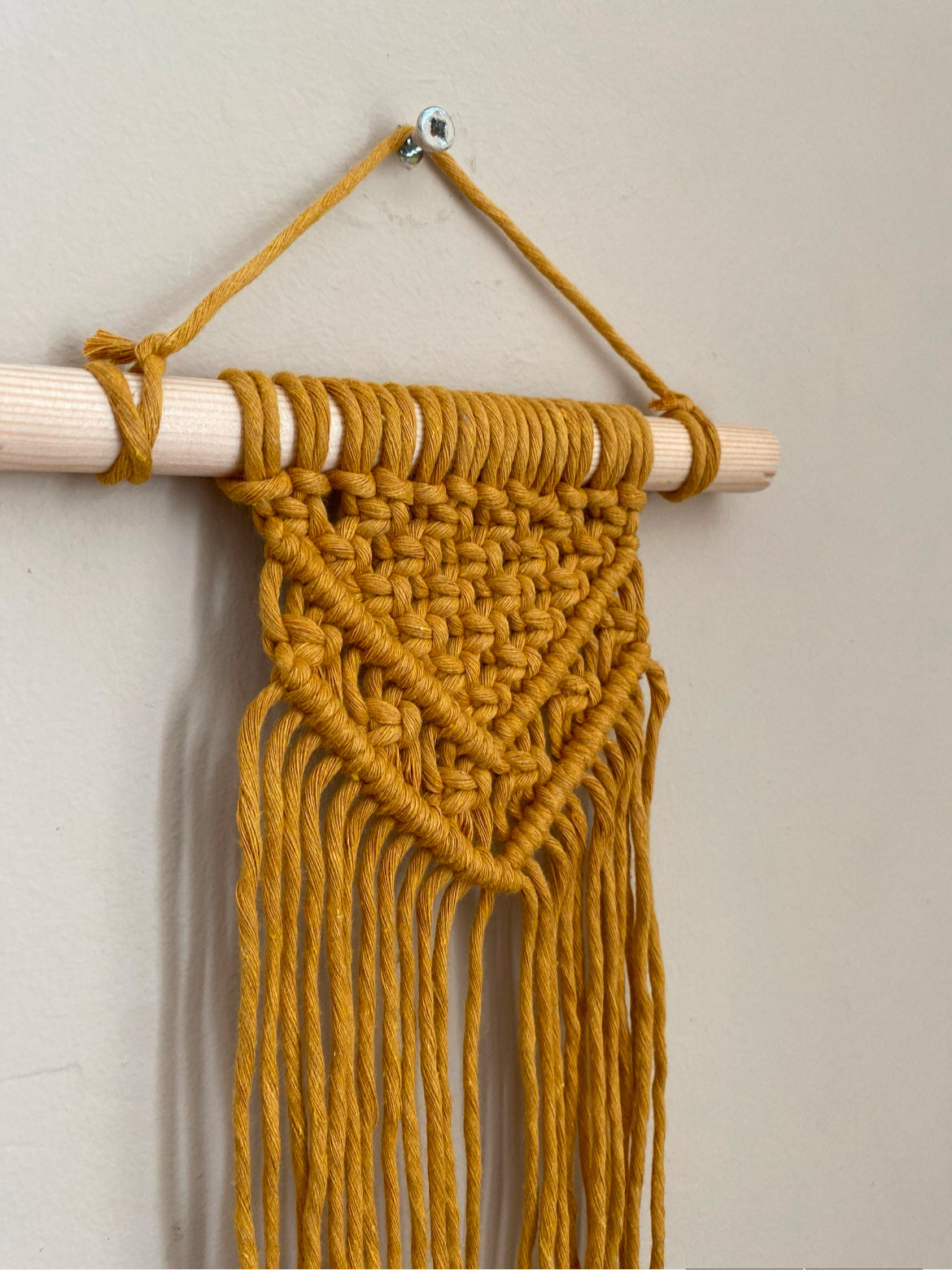 Handmade macrame wall hanging made with mustard yellow recycled cotton yarn on a solid wooden dowel.
