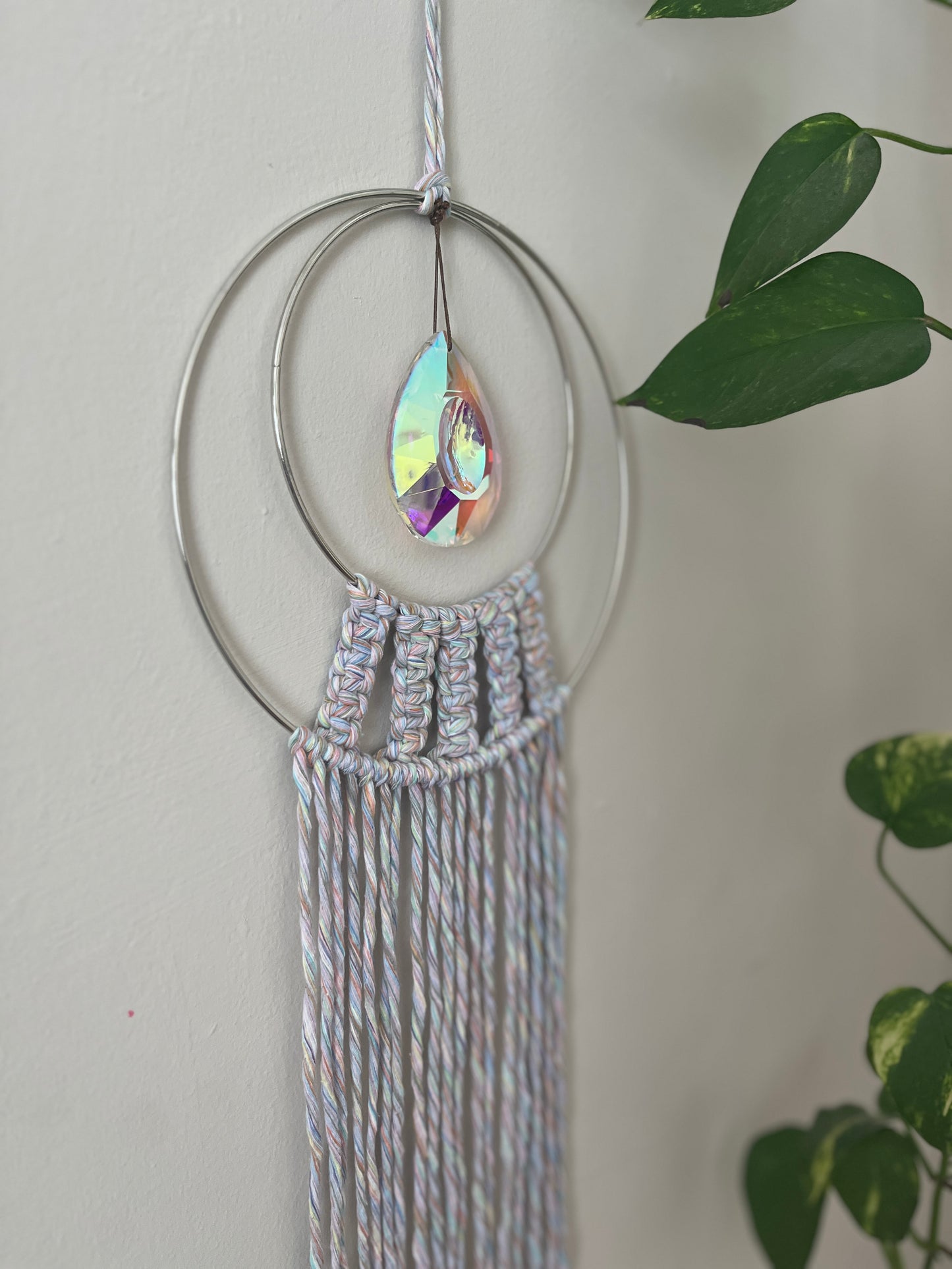 Handmade macrame Suncatcher made with pastel coloured recycled yarn, on two metal hoops, with a large hanging crystal in the centre.