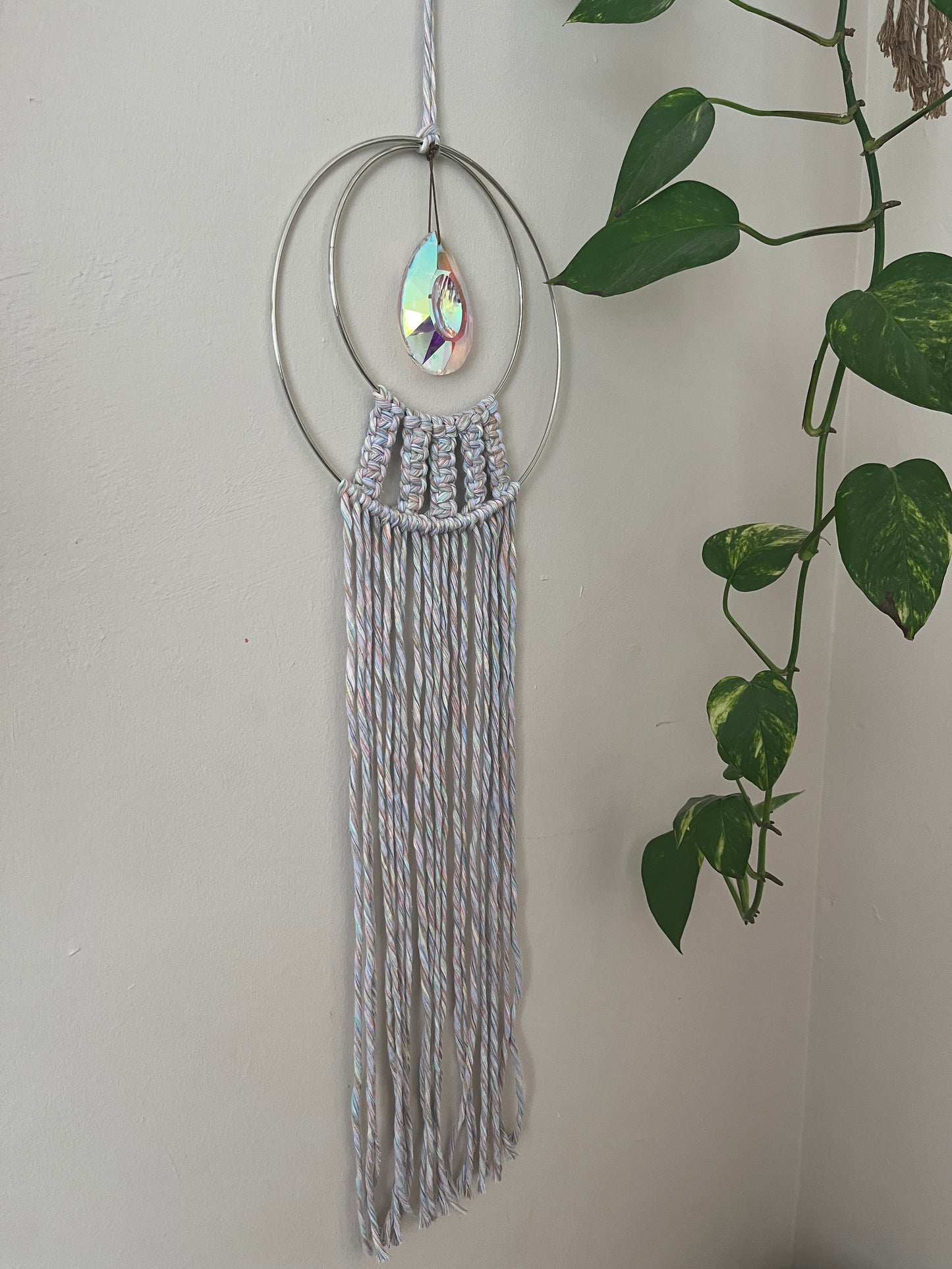 Handmade macrame Suncatcher made with pastel coloured recycled yarn, on two metal hoops, with a large hanging crystal in the centre.