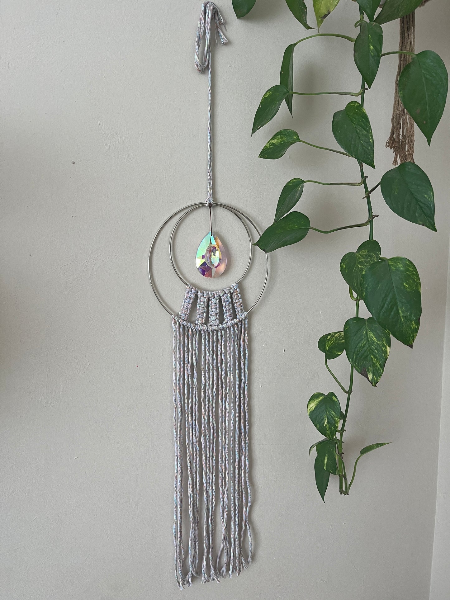 Handmade macrame Suncatcher made with pastel coloured recycled yarn, on two metal hoops, with a large hanging crystal in the centre.