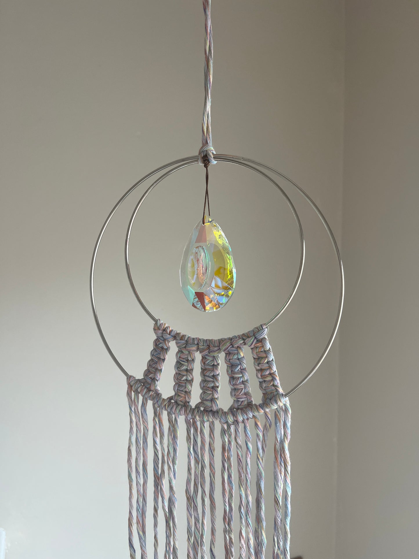 Handmade macrame Suncatcher made with pastel coloured recycled yarn, on two metal hoops, with a large hanging crystal in the centre.