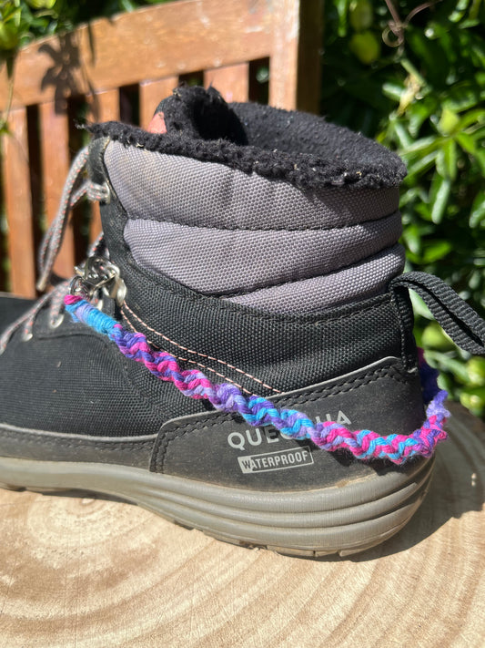 A pair of knotted chain style boot charms made with recycled cotton yarn. Shown attached to a pair of black walking boots.