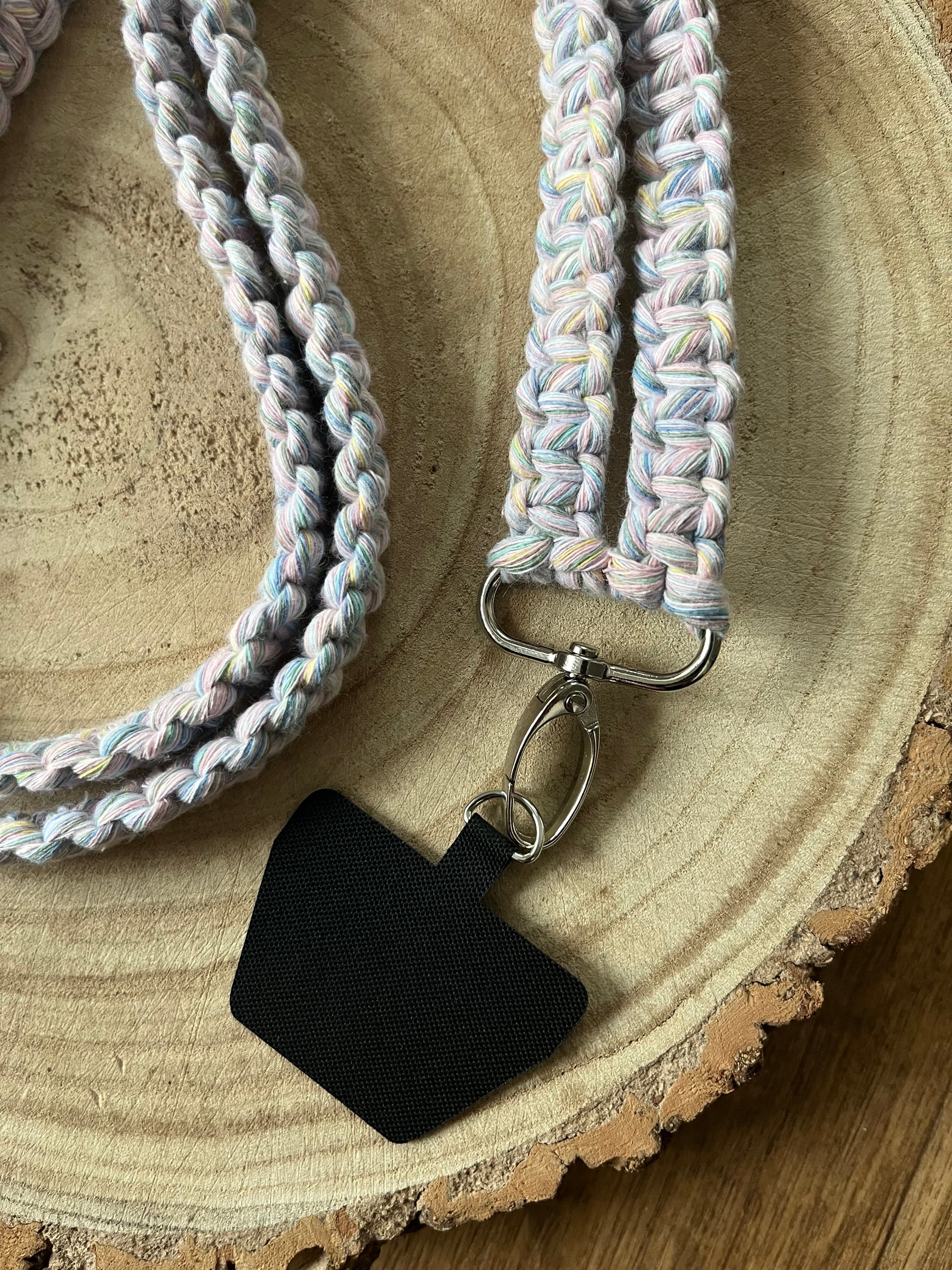 Close up of the metal clasp and universal phone tether on the end of a long crossbody phone strap made with pastel yarn.