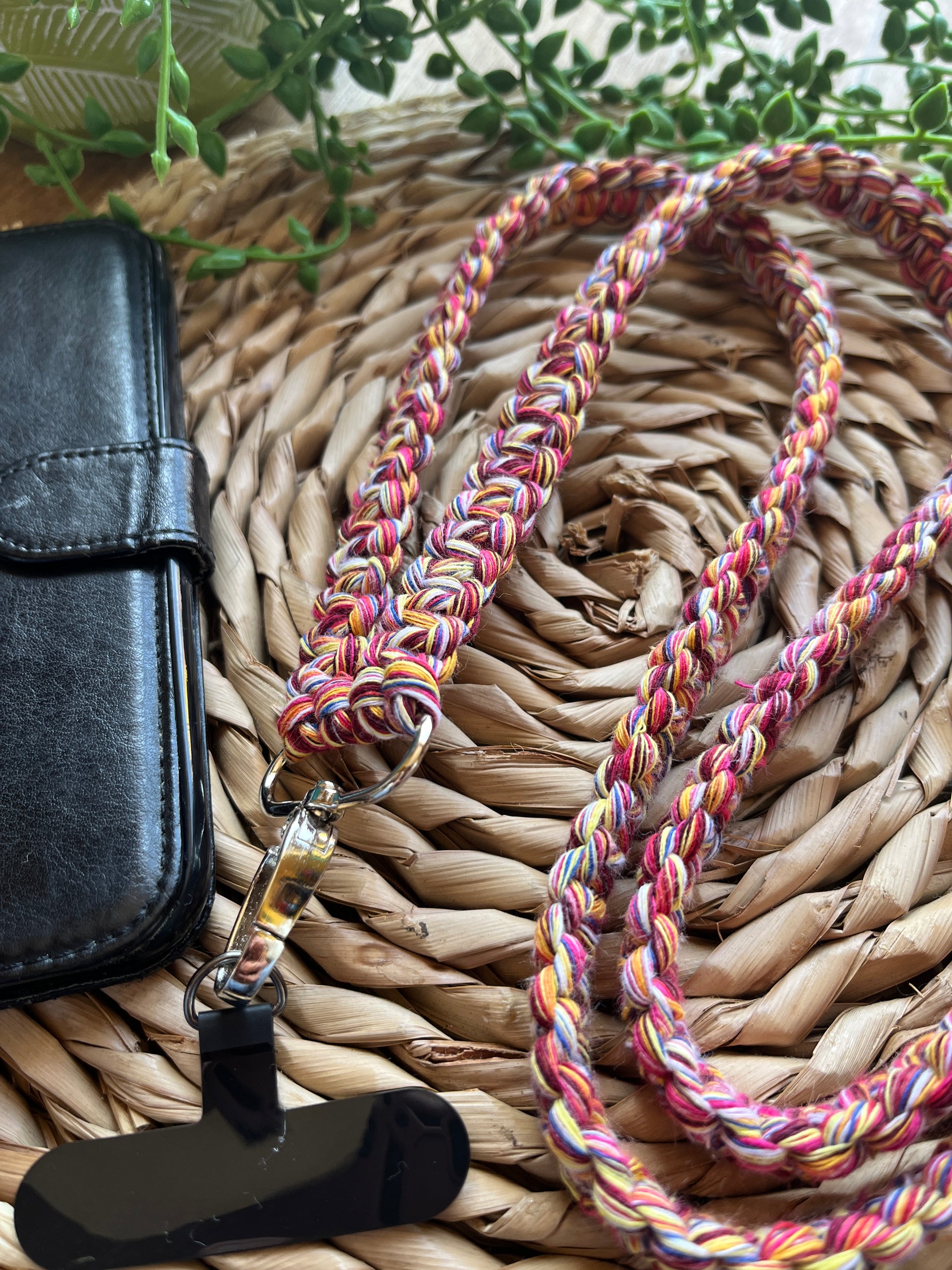 A long crossbody phone strap made with multicoloured yarn, and metal clasp attached to a black phone tether tab.