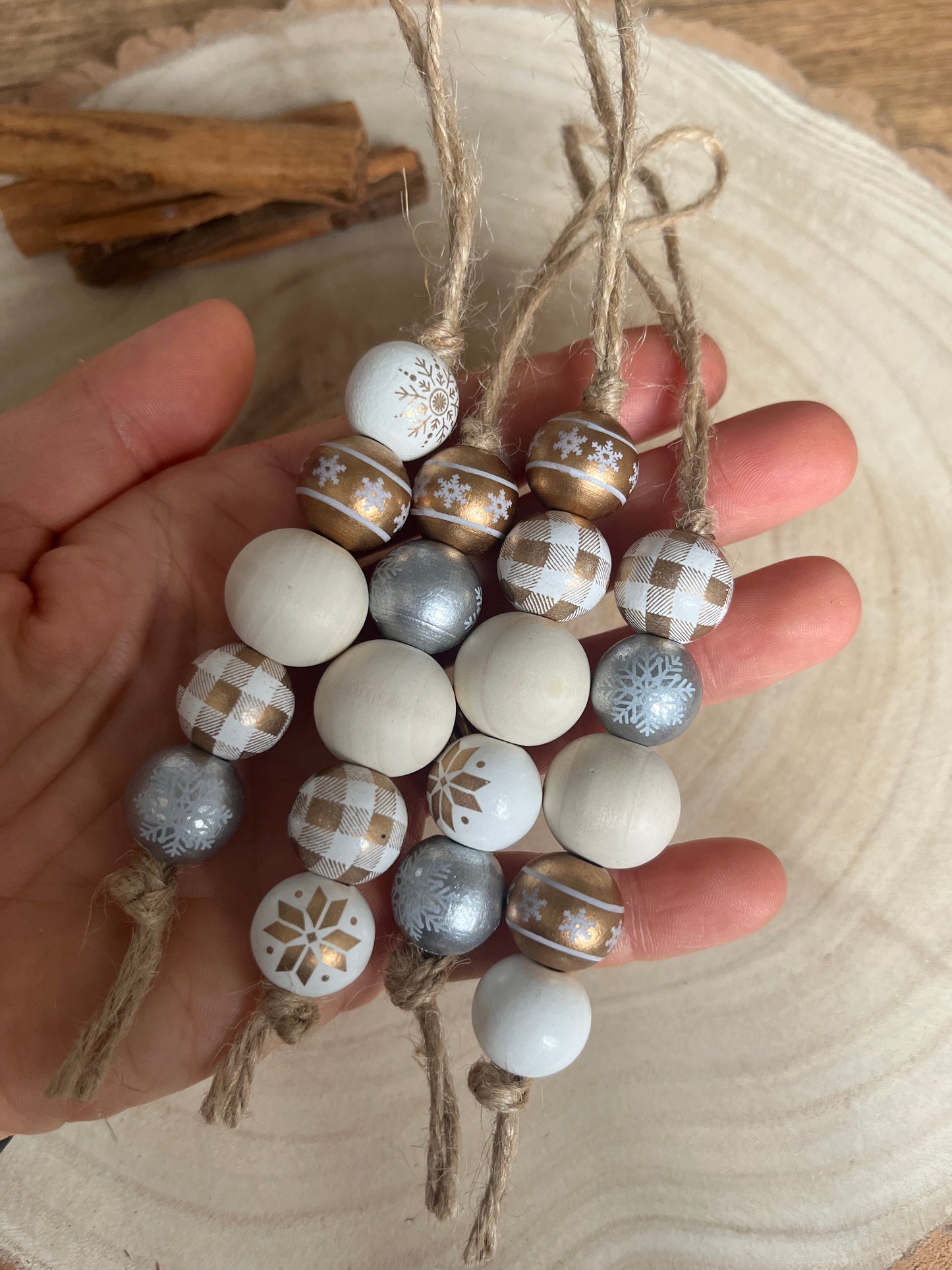 Hand holding a decorative garland with white, silver, and gold beads on a wooden surface.