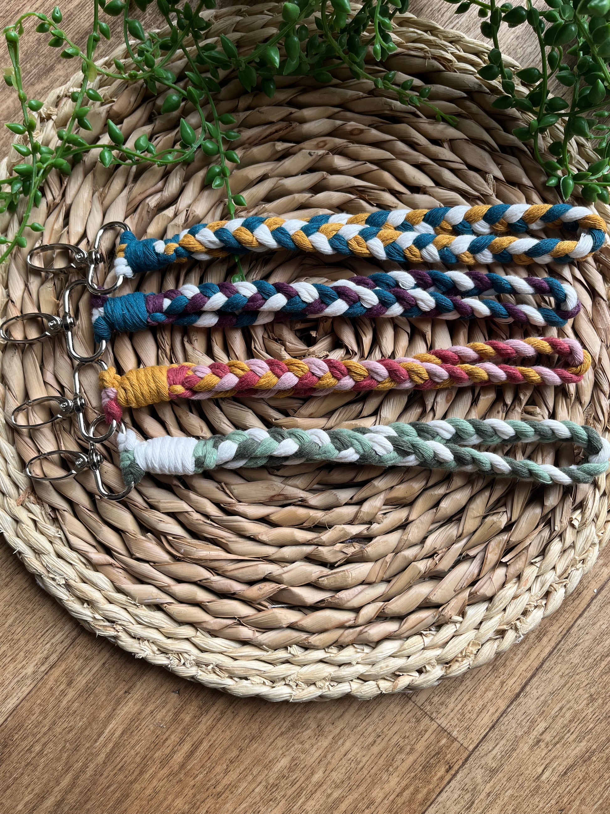 A photo of four handmade macrame braided wristlets, laid on a wicker mat. The wristlets are made with different colour combinations of recycled cotton, with metal lobster clasps.
