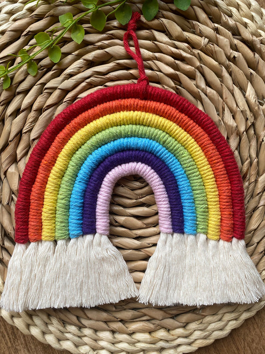 Colourful macrame rainbow hanging on a woven mat.