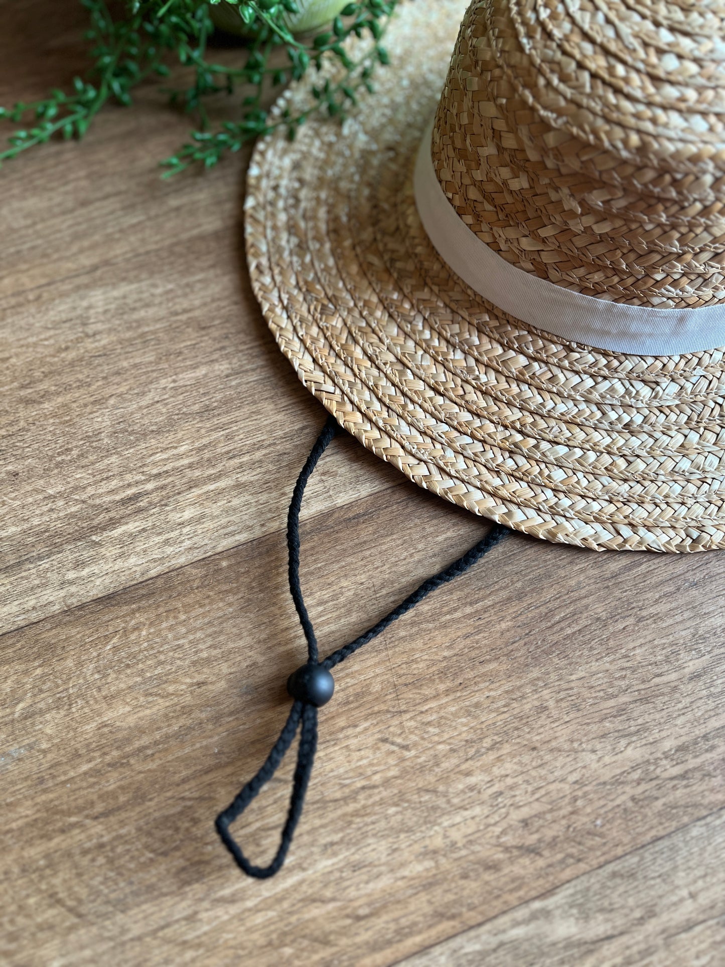 Straw hat with a black chin strap on a wooden surface