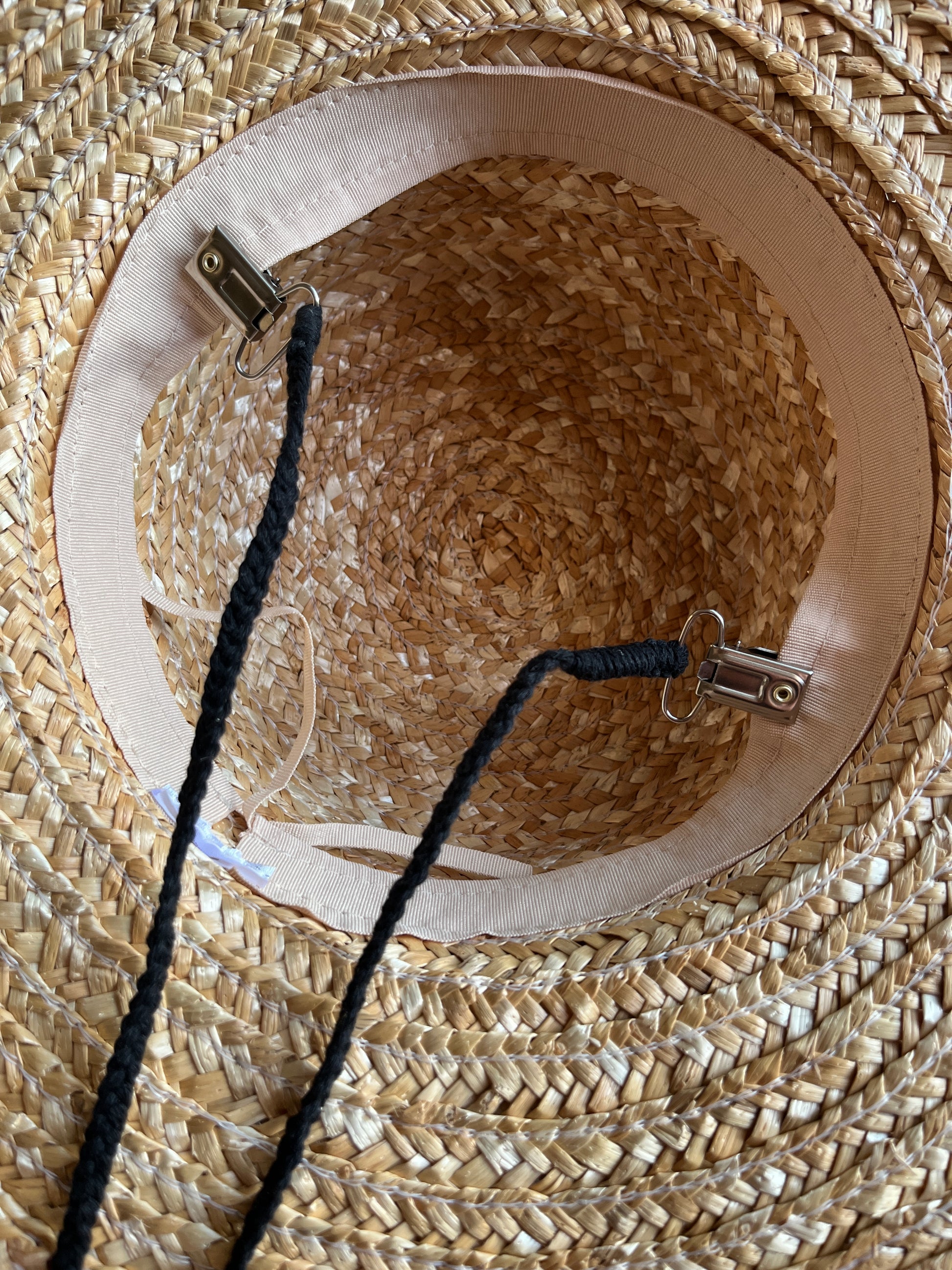 Close-up of the inside of a straw hat with a black chin strap cord attached to the inside band with metal clips.