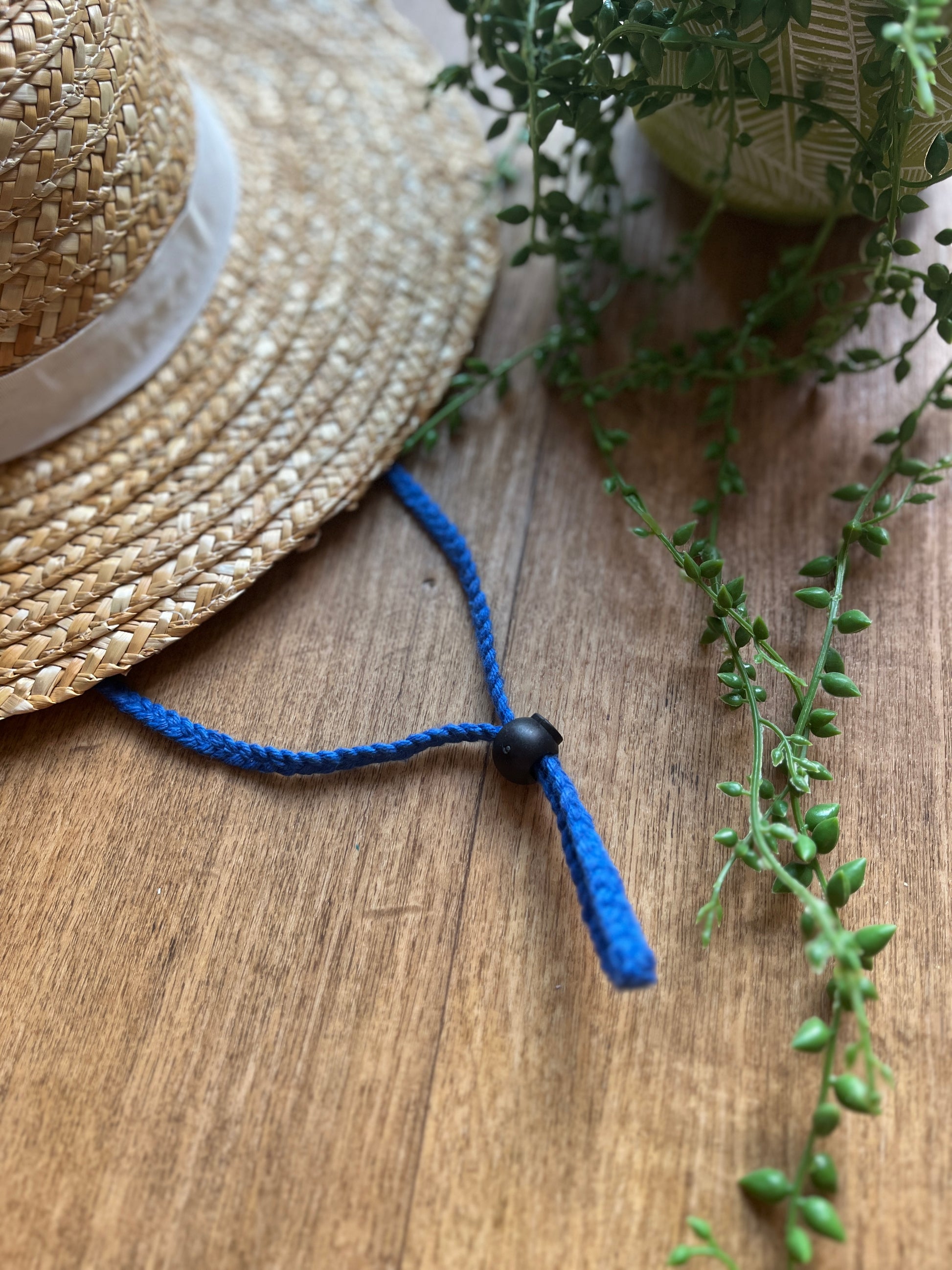 Straw hat with a blue chin strap cord on a wooden surface
