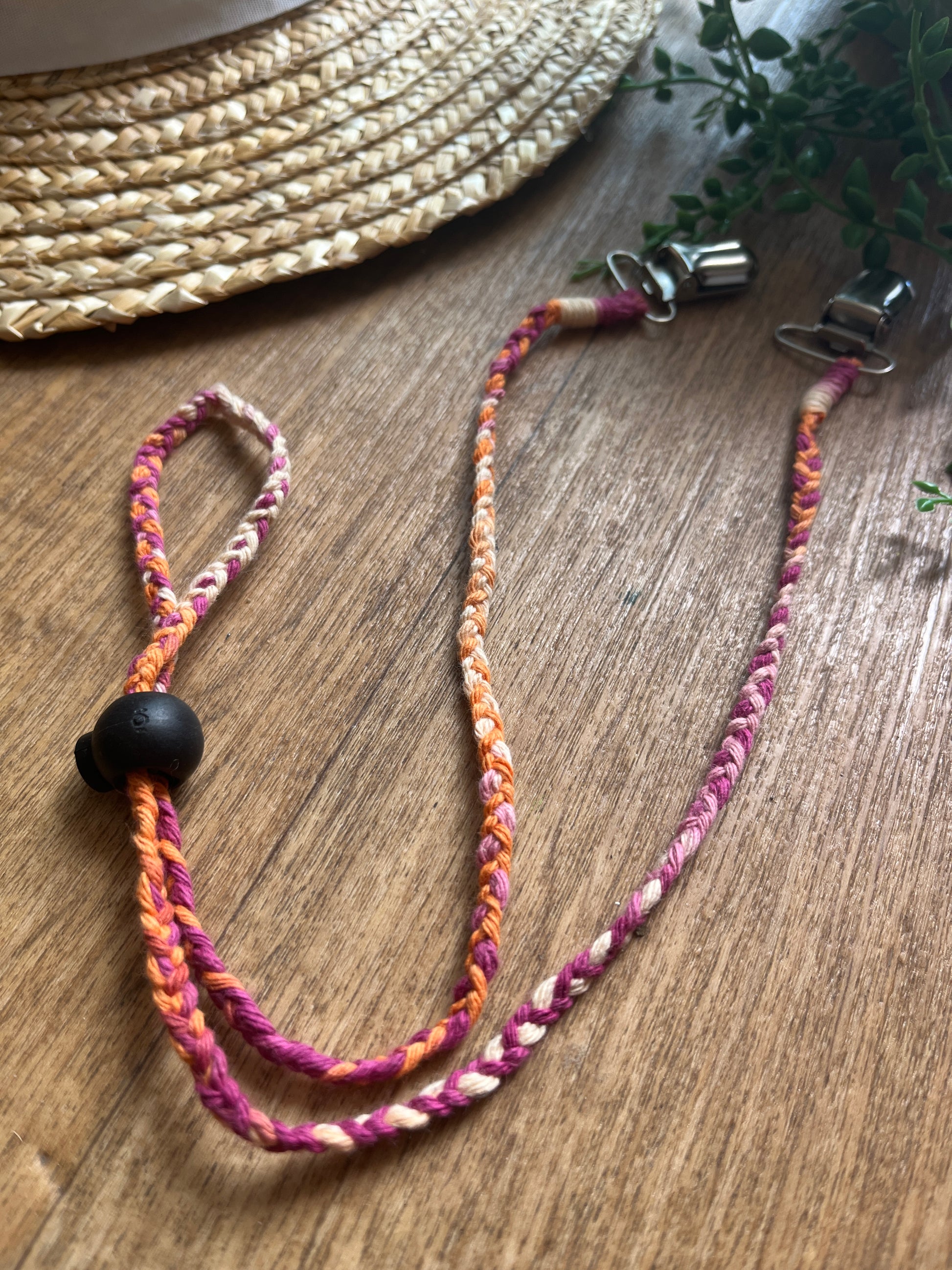 Multicoloured braided chin strap lanyard with a black toggle and metal clips, on a wooden surface