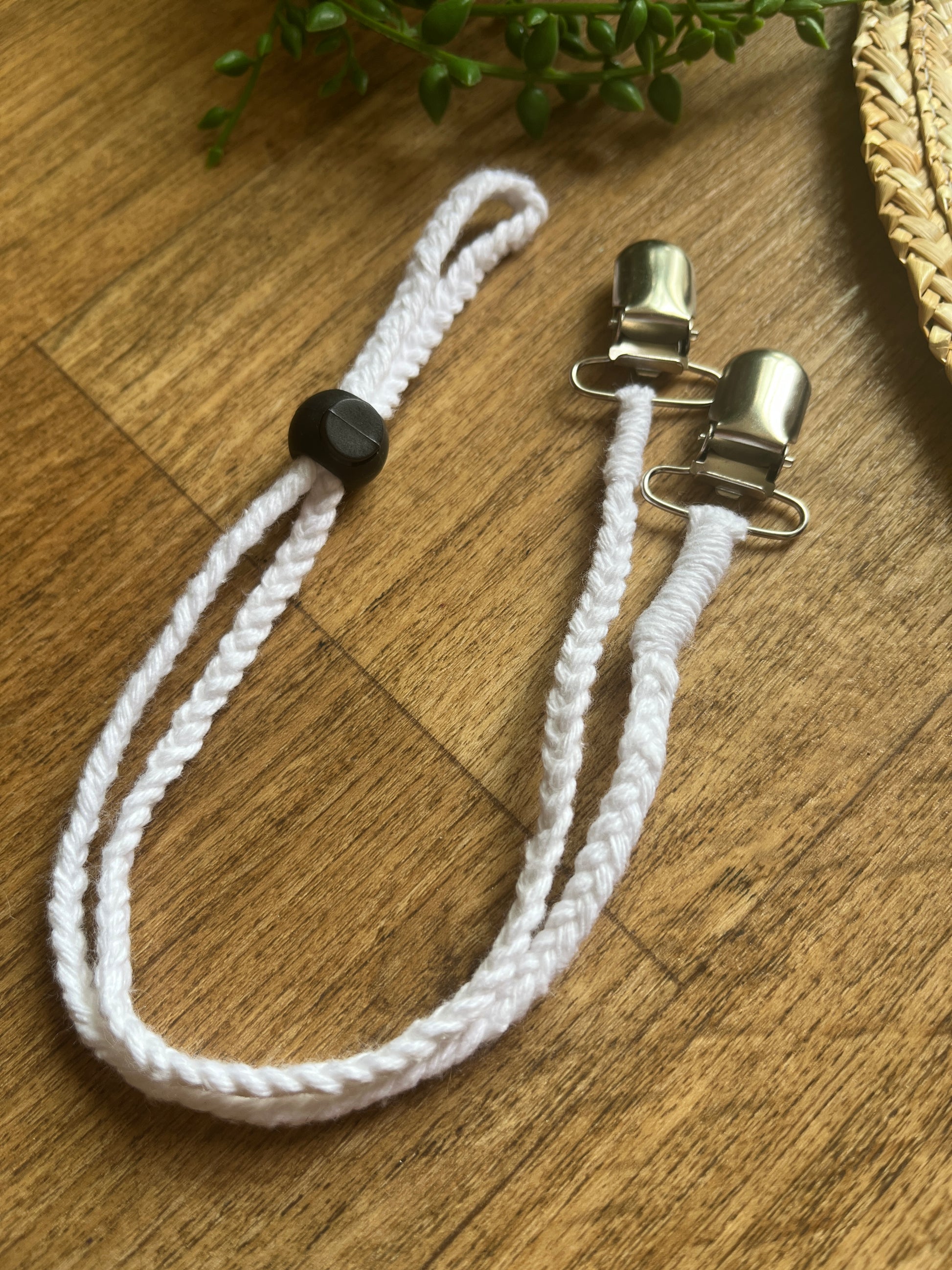 White chin strap lanyard with metal clips and a black toggle on a wooden surface