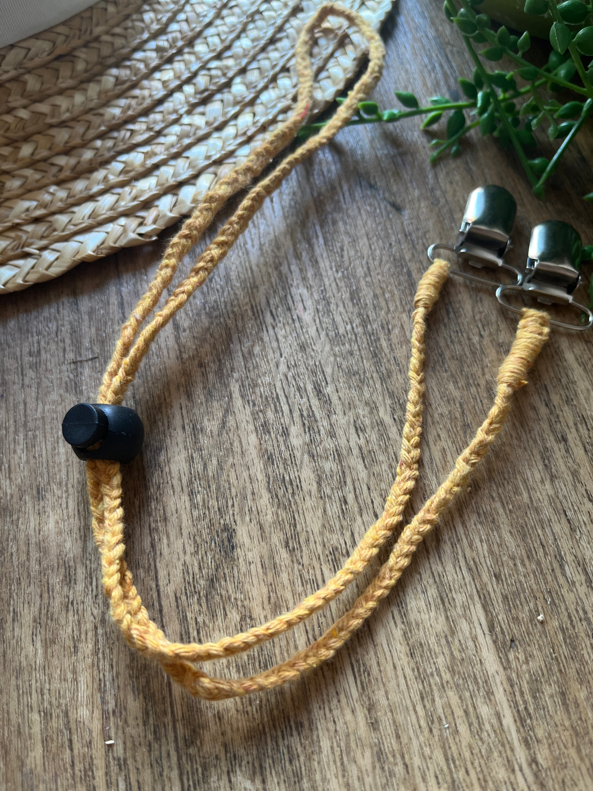 Braided yellow macrame chin strap with a black toggle and metal clips on a wooden surface