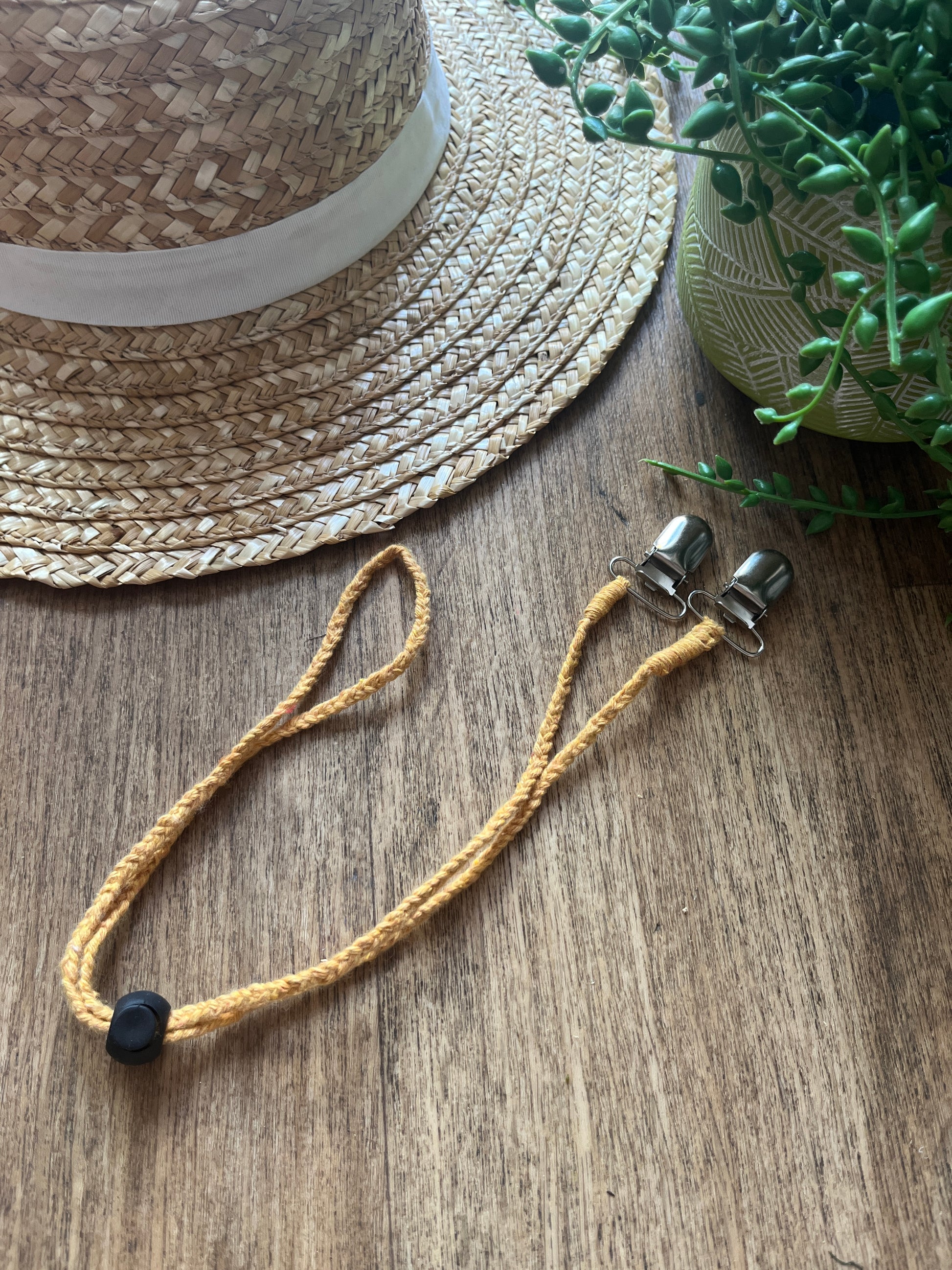 Straw hat on a wooden surface with a yellow chin strap placed next to it.