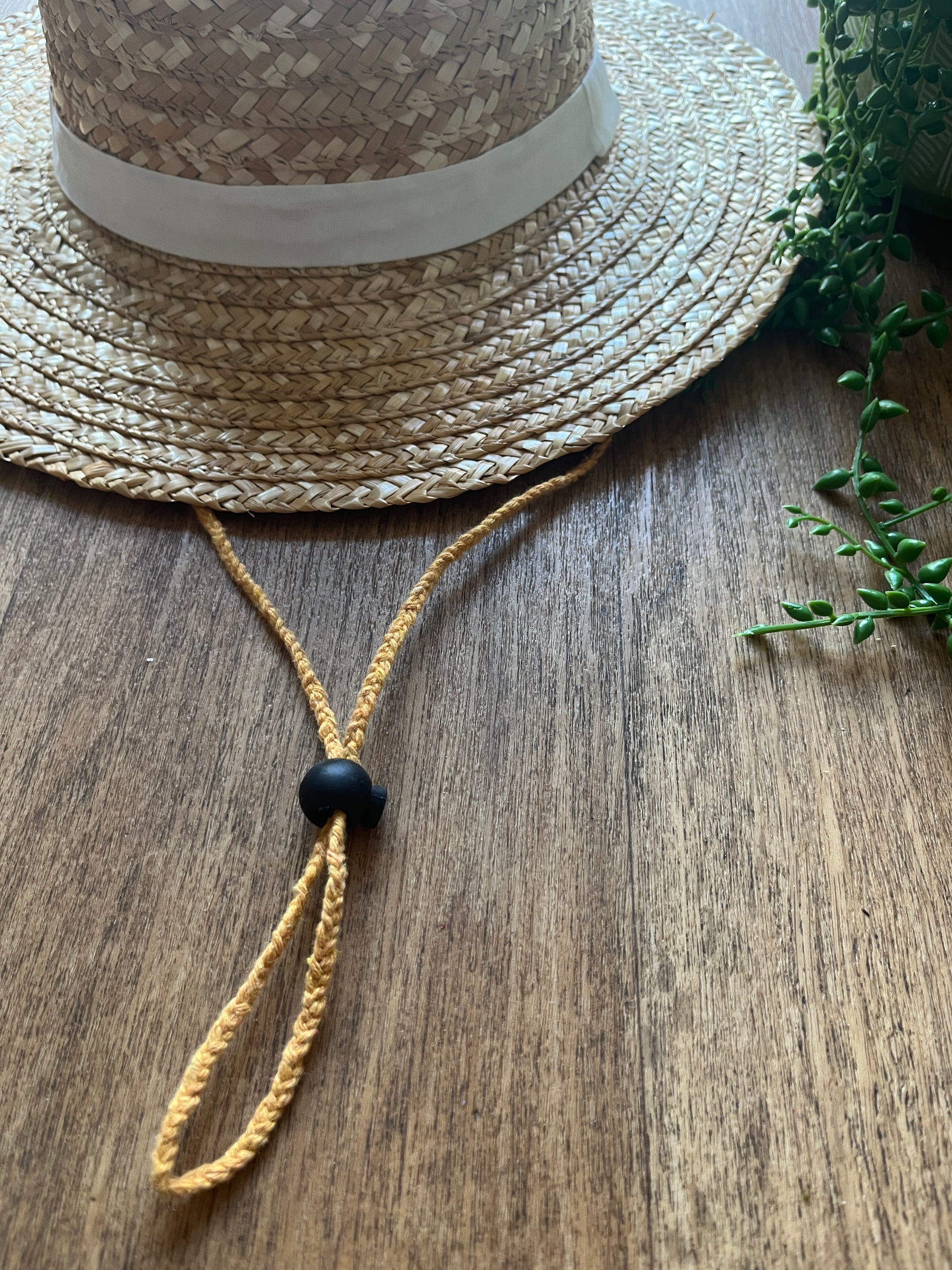 Straw hat with a braided yellow chin strap string with black toggle on a wooden surface