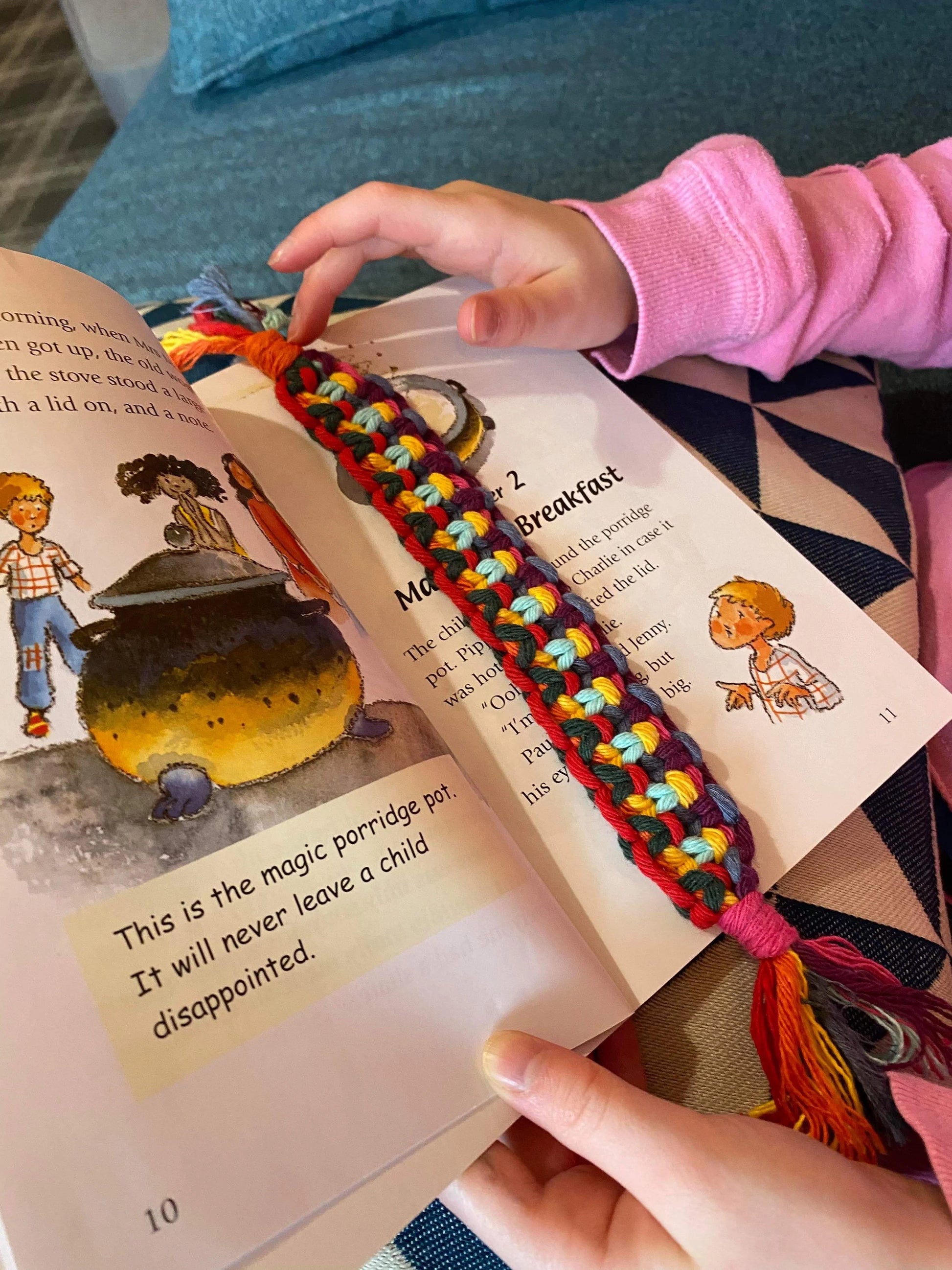 Handmade macramé bookmark with knotted design made with rainbow colour of recycled cotton, laid across an open children's book.