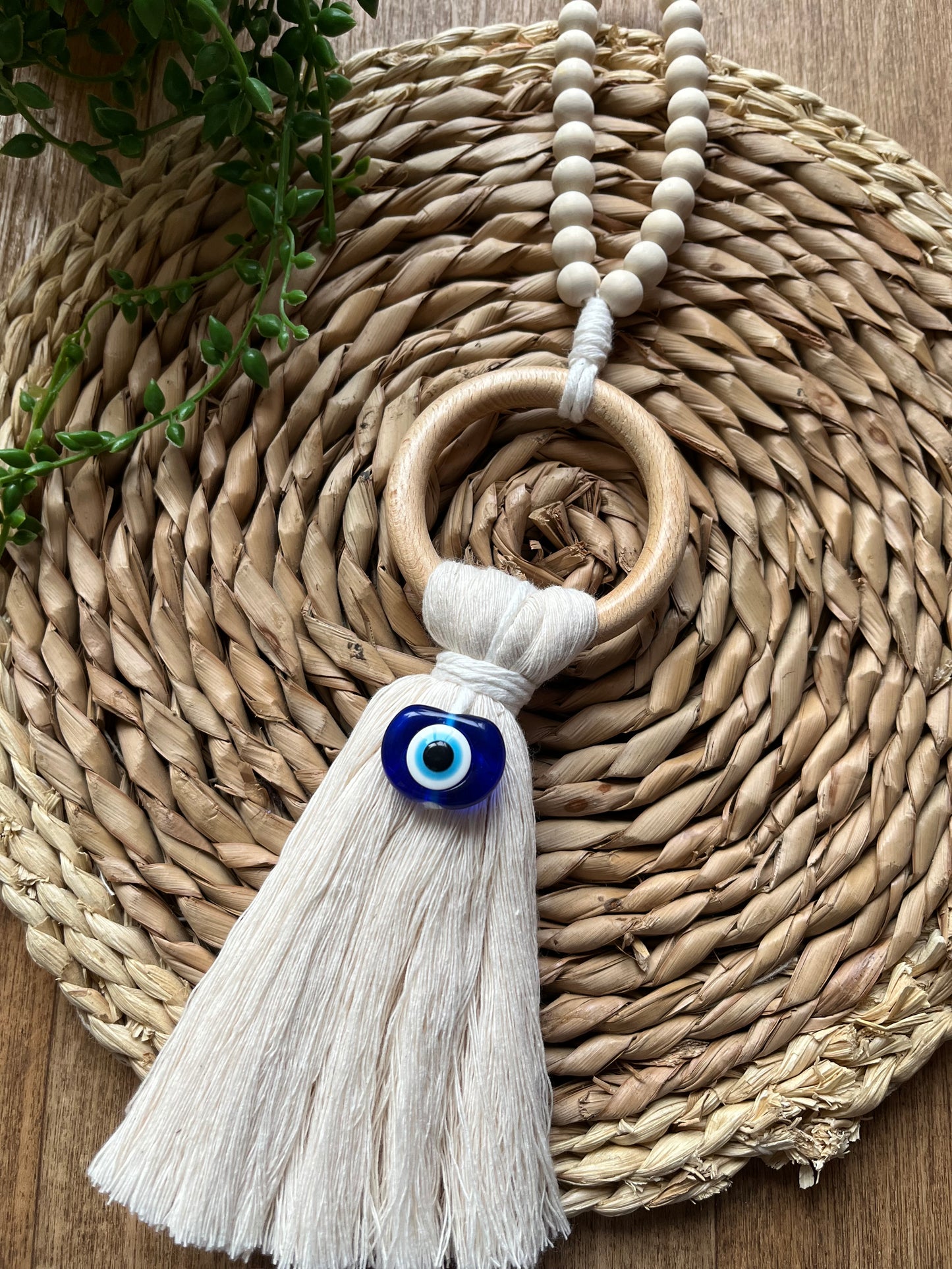 Handmade macrame door hanger, made with recycled cotton, on a wooden ring, with a blue resin evil eye bead and beaded hanging loop.