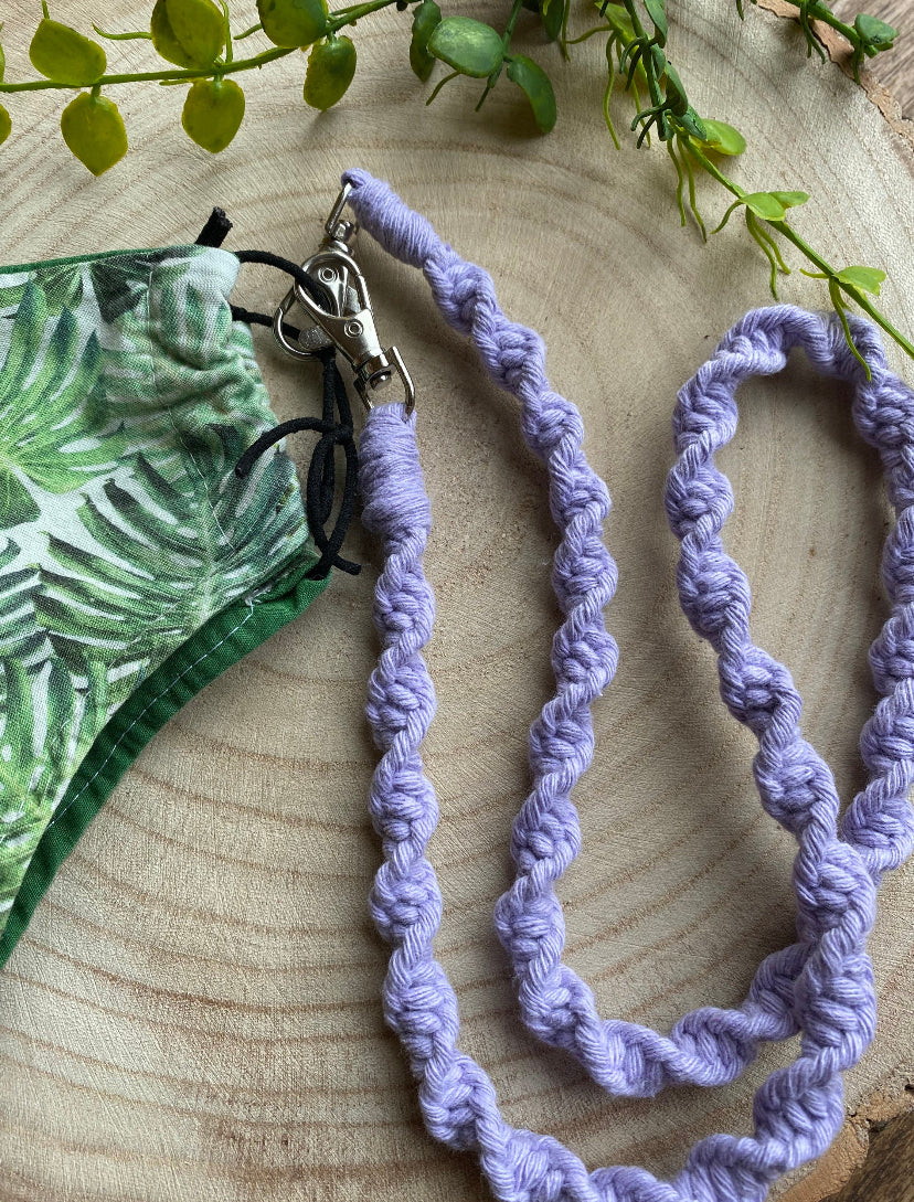 Handmade macramé face mask lanyard in lilac cotton cord attached by small metal clips on to a face mask which has a green leafy print.