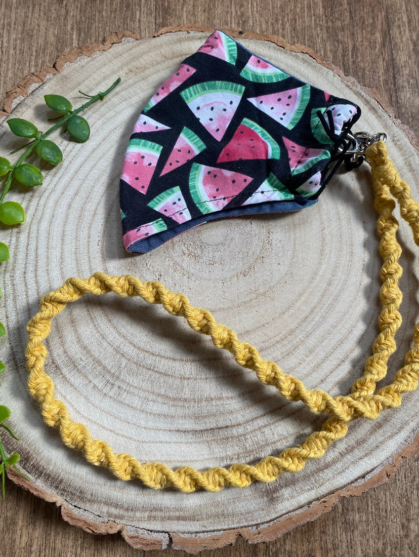 Handmade macramé face mask lanyard in mustard yellow cotton cord attached by small metal clips on to a face mask which has a watermelon print.