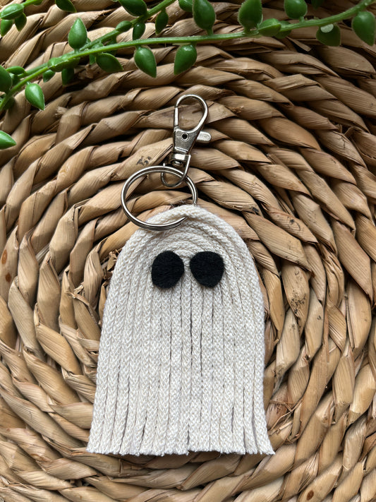 White yarn ghost keychain with black eyes and a silver keyring clasp, laid out on a woven mat