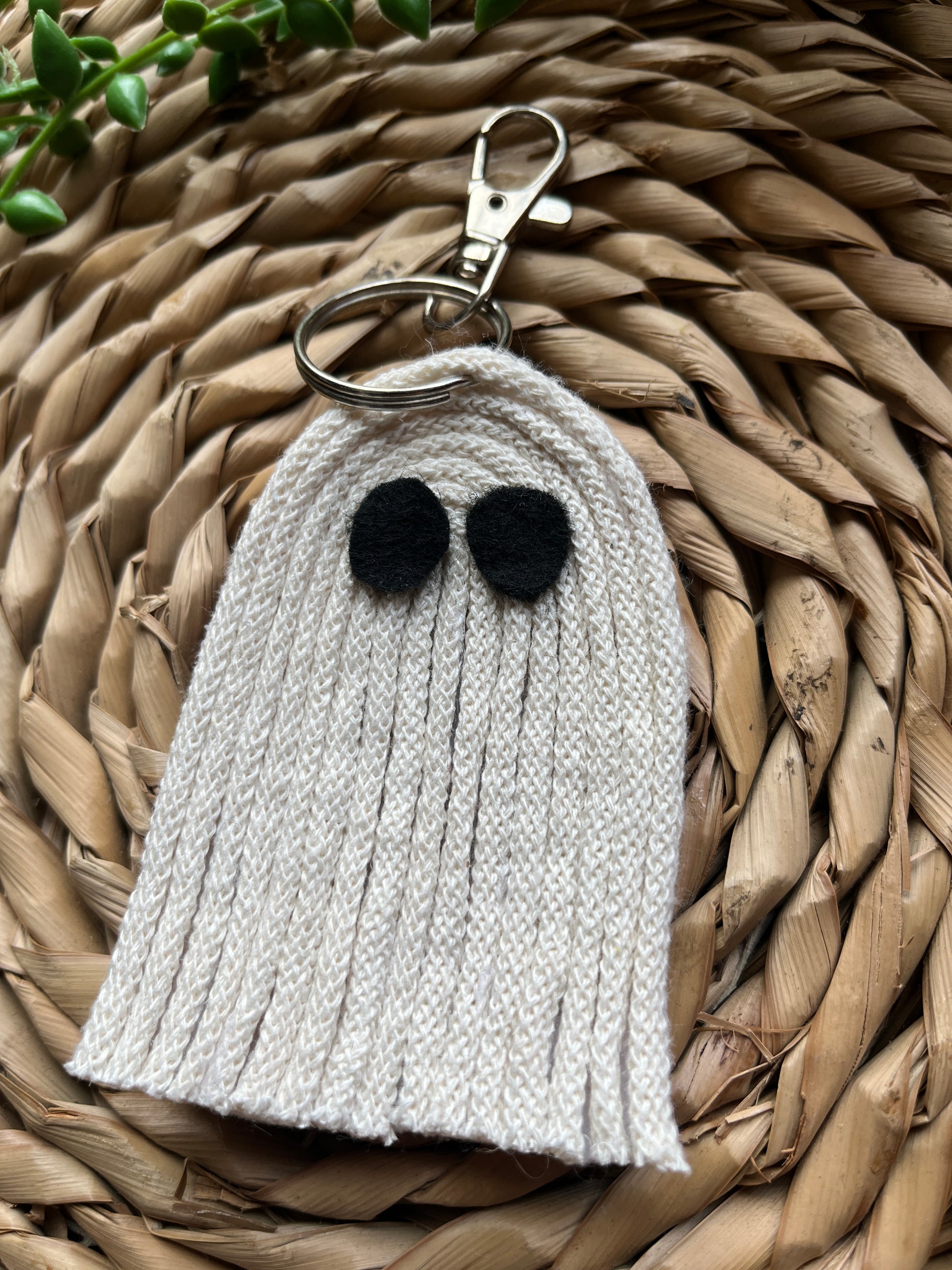 White ghost-shaped keychain with black dots on a woven surface