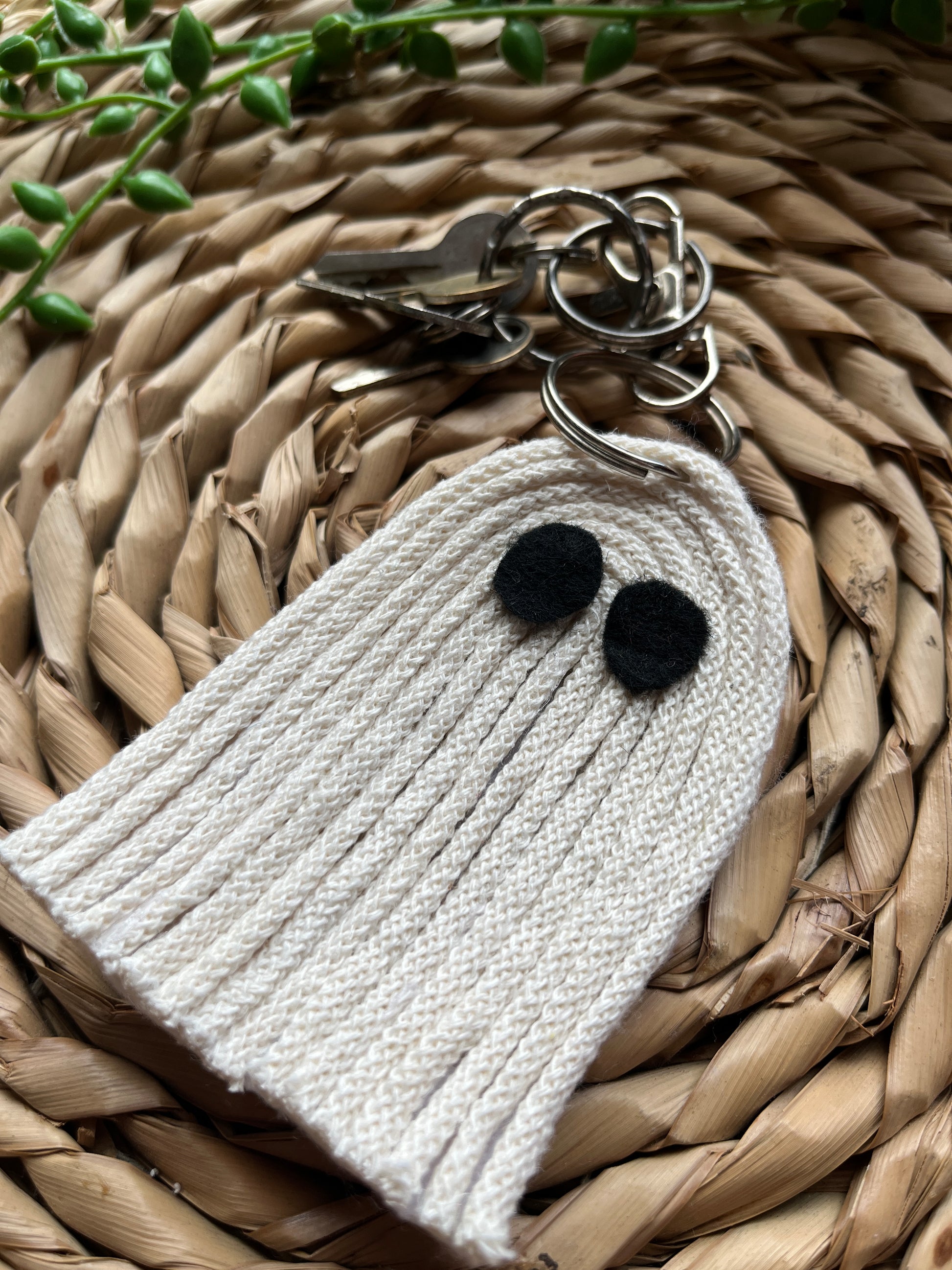 Close up of a white ghost-shaped keychain with black dot eyes on a woven surface