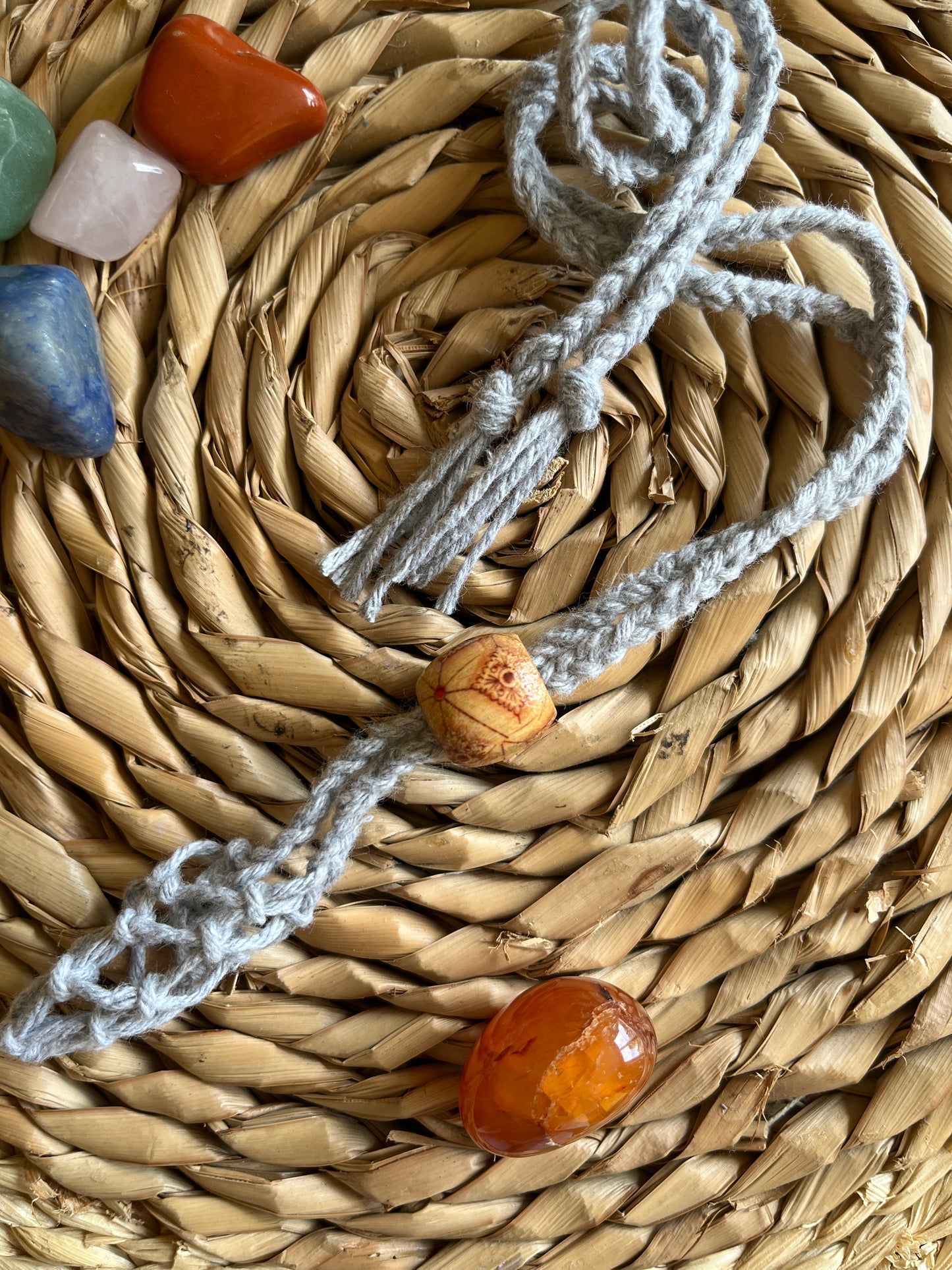 Macrame Gemstone Holder net pouch made with grey eco friendly recycled cotton and a Wooden bead. There are 5 loose gemstones displayed next to the gemstone holder.