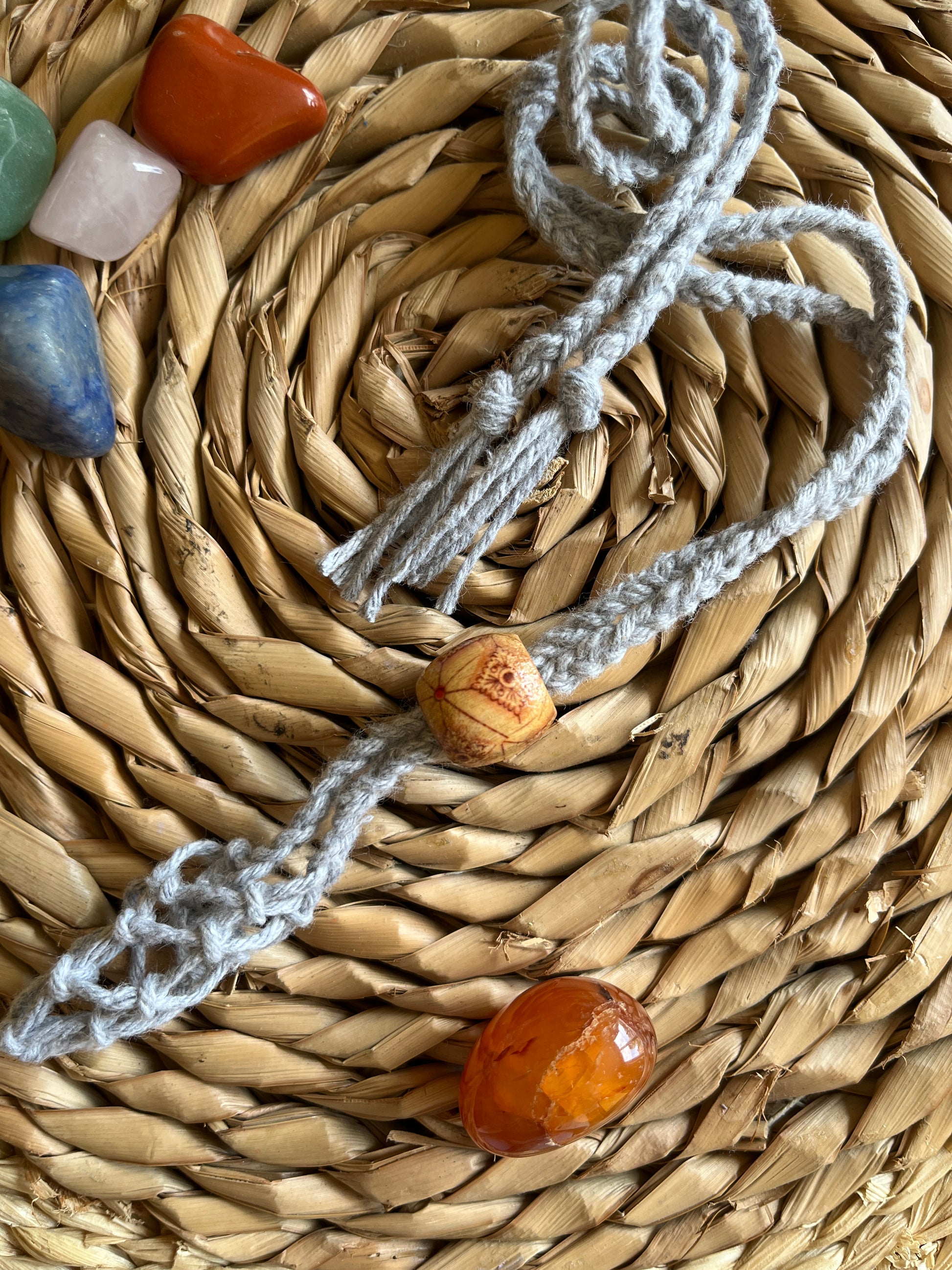 Macrame Gemstone Holder net pouch made with grey eco friendly recycled cotton and a Wooden bead. There are 5 loose gemstones displayed next to the gemstone holder.