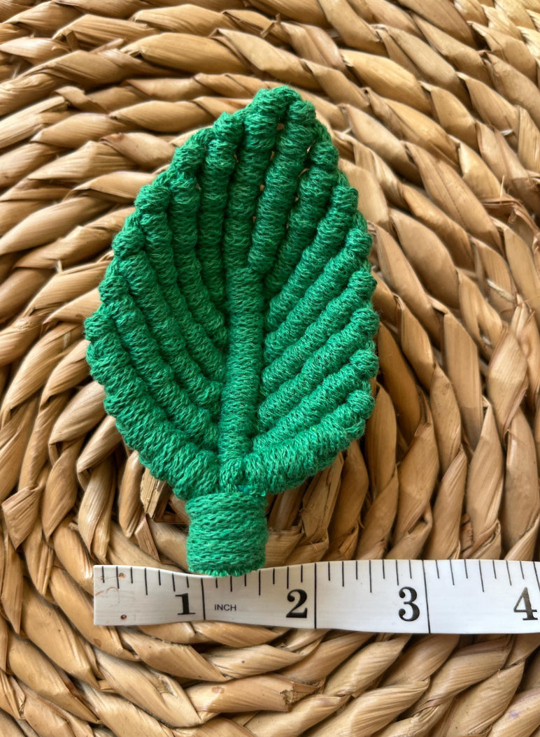 Green leaf-shaped embellishment on a woven surface with a ruler for scale.