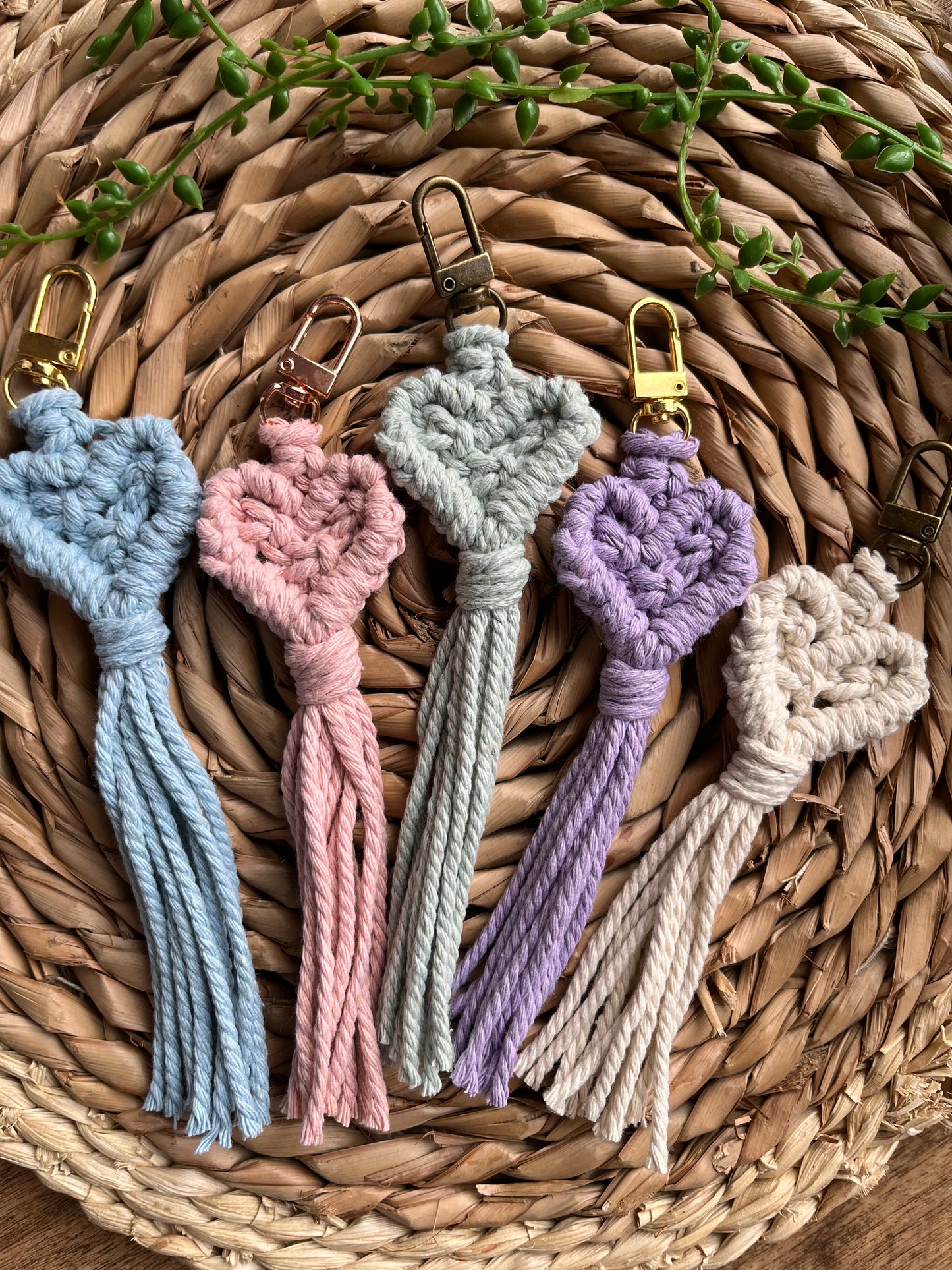 Handmade heart shaped small macrame keychains. The image shows five keychains laid on a wicker surface, in a variety of pastel shades.