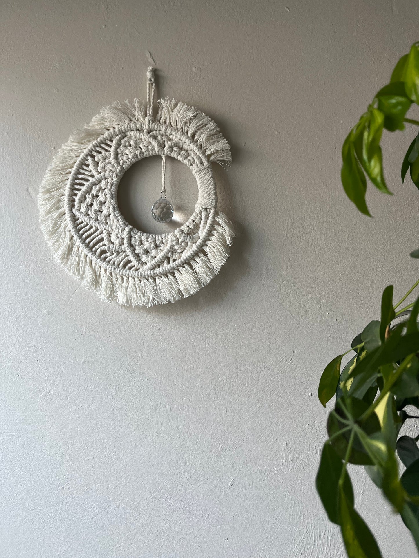 Handmade macrame moon shaped boho sun catcher made with recycled cotton natural yarn and a crystal prism in the centre.
