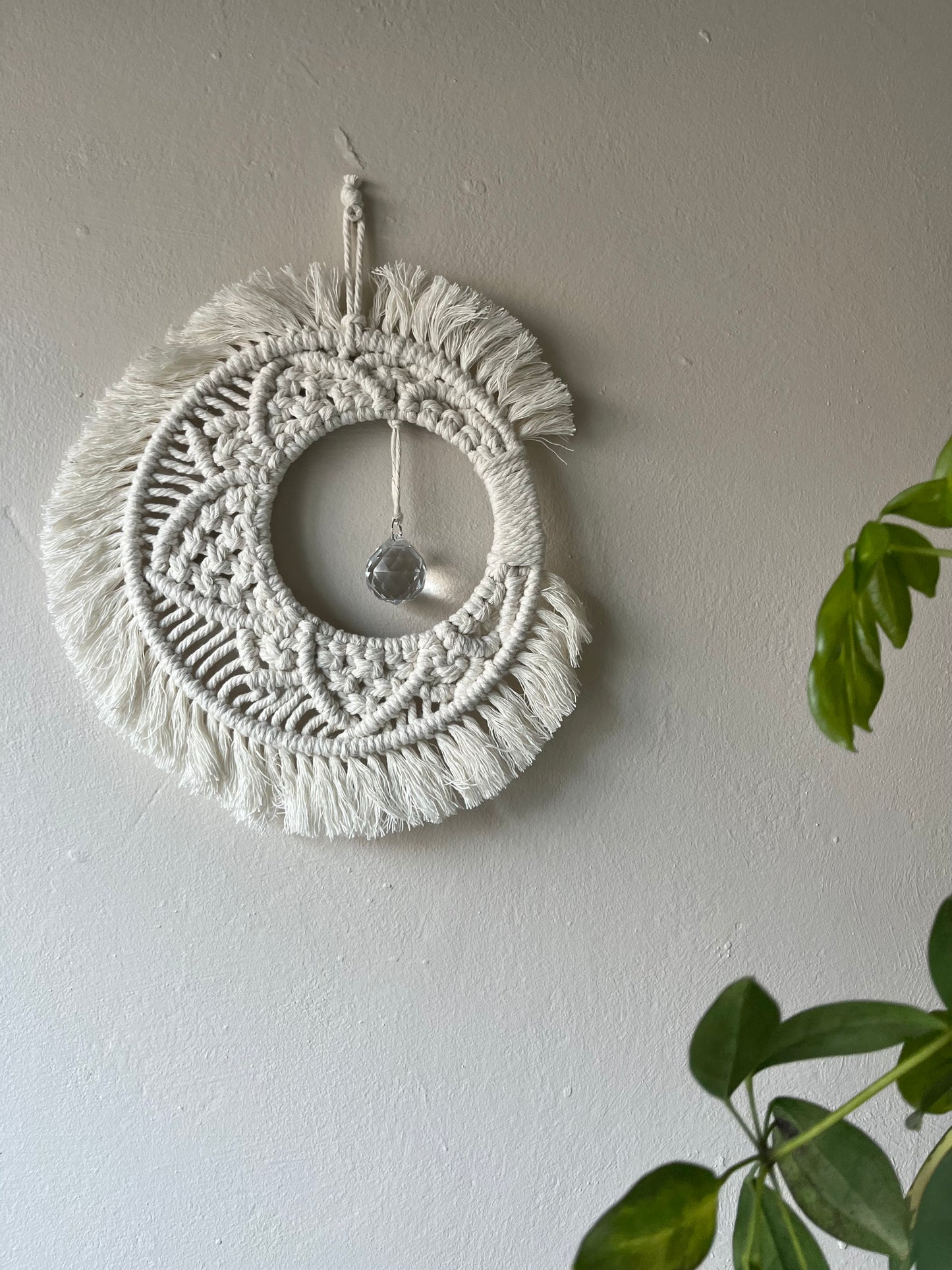 Handmade macrame moon shaped boho sun catcher made with recycled cotton natural yarn and a crystal prism in the centre.