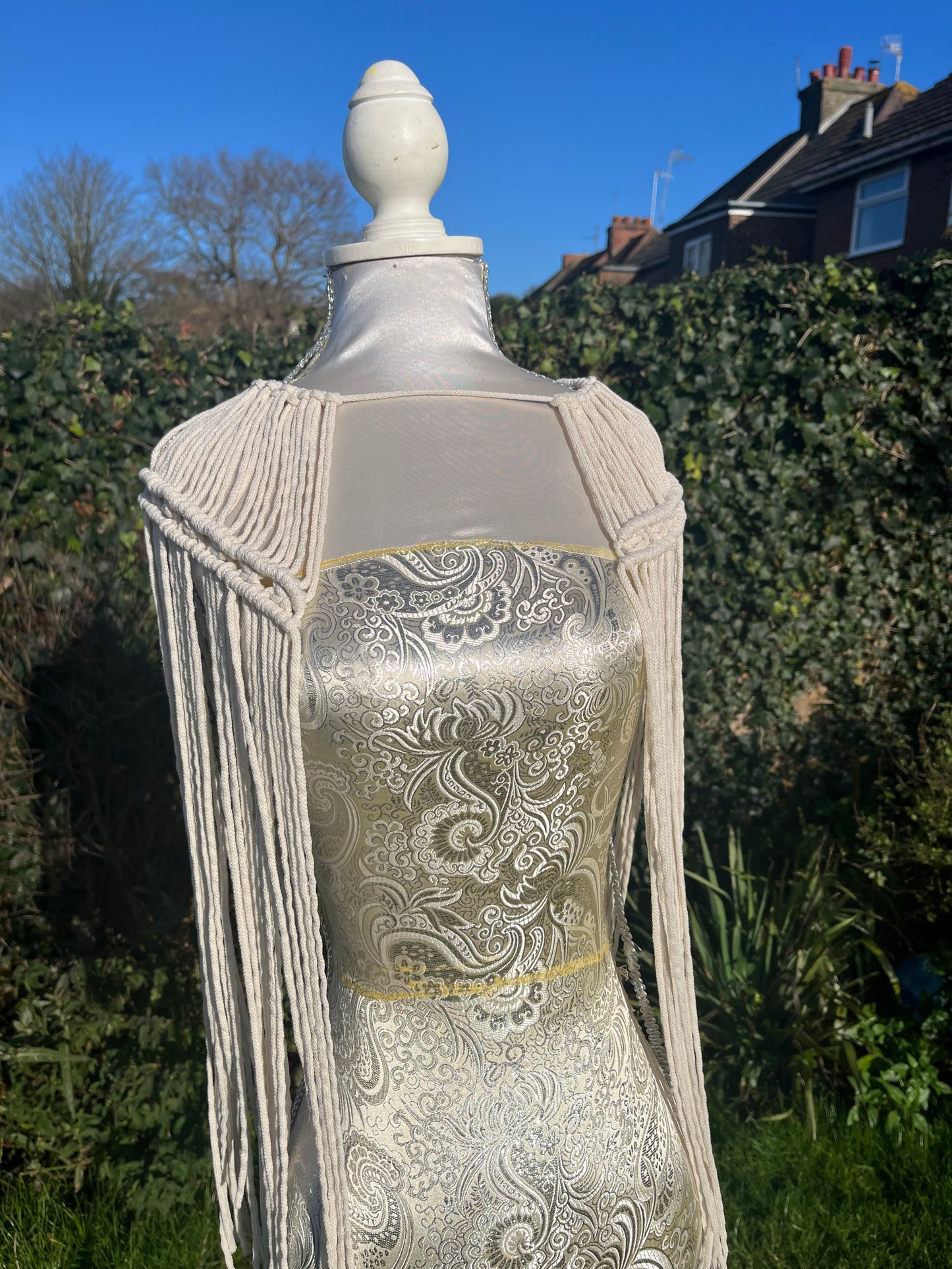 A mannequin outside in the sunshine displays a handmade macrame shoulder accessory epaulette made with recycled natural cotton